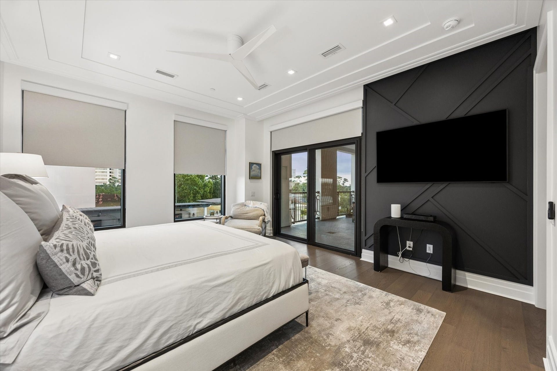 6017 Memorial Drive, #505, Houston, TX 77007 The primary suite offers an exceptional blend of privacy, sophistication, and indoor-outdoor living. A dramatic dark accent wall with geometric detailing creates a striking focal point, while elegant tray ceilings, engineered hardwood flooring, and expansive windows enhance the refined atmosphere. Glass doors open directly onto the private fifth-floor terrace, offering a seamless connection to outdoor living and beautiful views of the surrounding landscape.