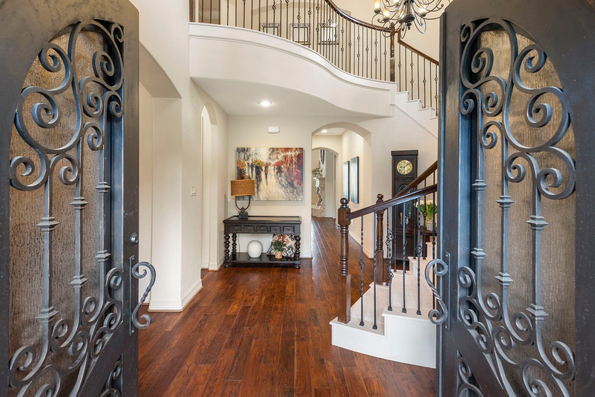 Grand two-story Foyer featuring arched iron double doors, rich wood flooring, and a dramatic chandelier that sets the tone for the homes timeless architectural elegance.