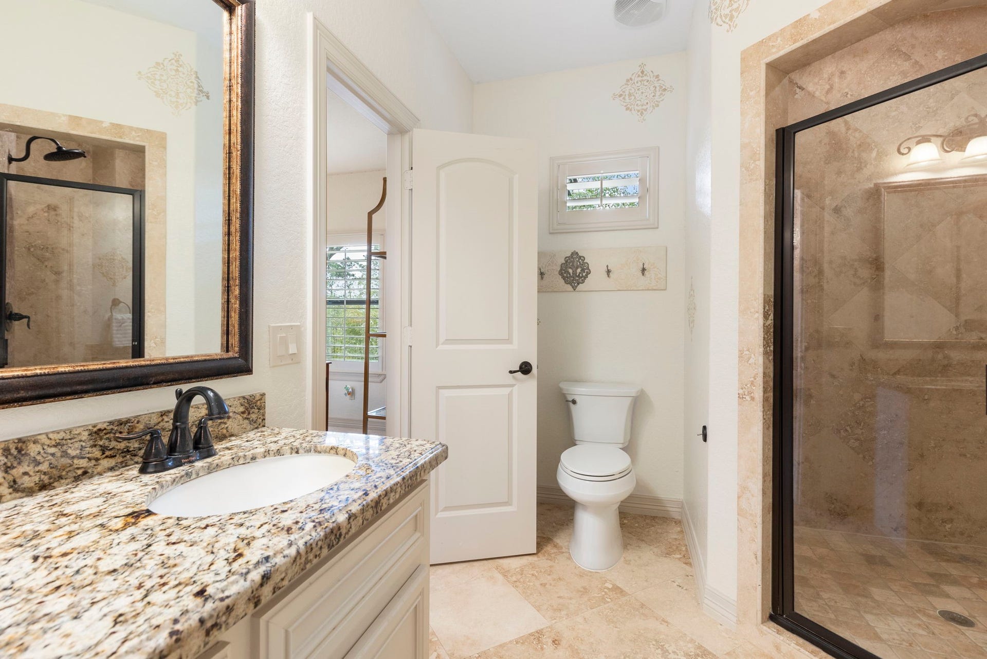 Private bath with Travertine flooring, oversized walk-in shower with bench seating, granite vanity with abundant storage, and a large framed mirror.