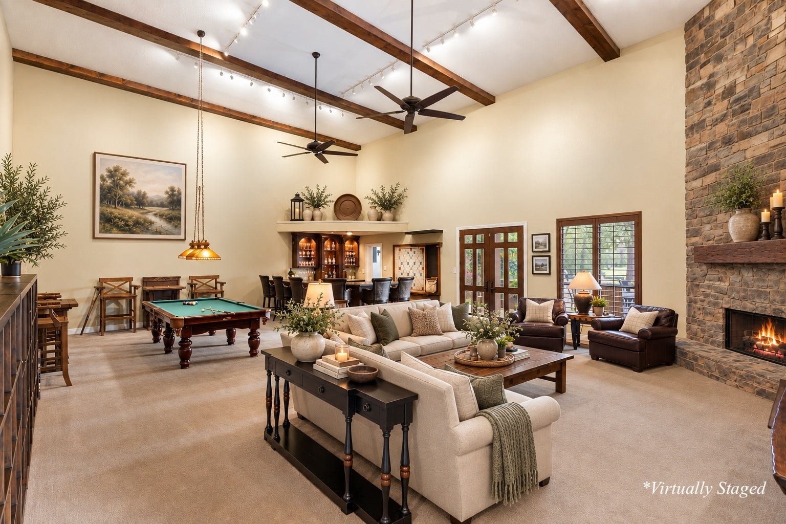 Nearly 1,200 SF Game & Trophy Lounge featuring soaring beam ceilings, floor-to-ceiling stone fireplace, full bar, integrated sound system, and French doors opening to the backyard. (*Partially Virtually Staged)