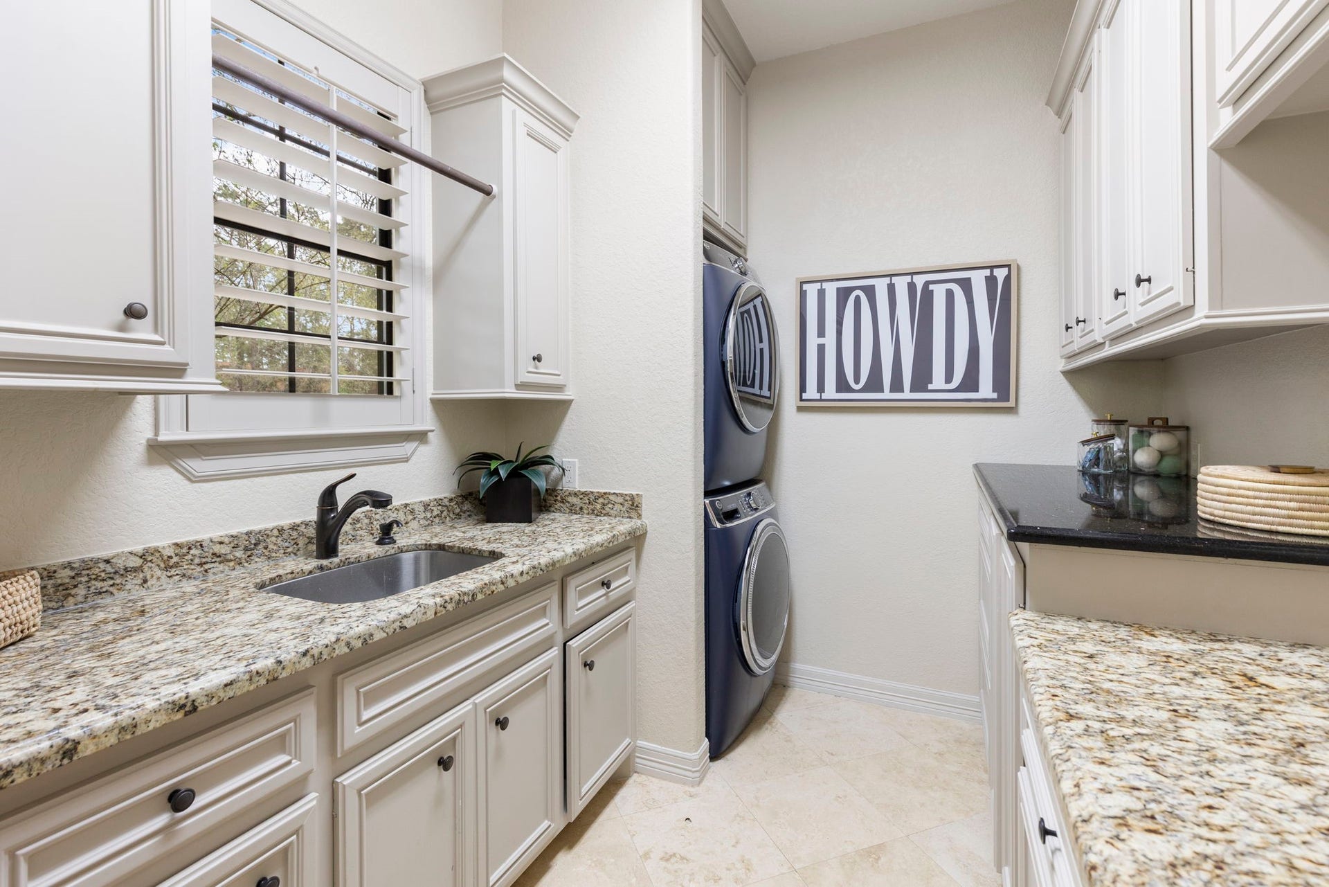 Spacious and thoughtfully designed Utility Room with extensive granite countertop workspace, custom built-ins on both sides, Travertine flooring, and a utility sink. Ideally situated off the side entry door to porte-cochere.