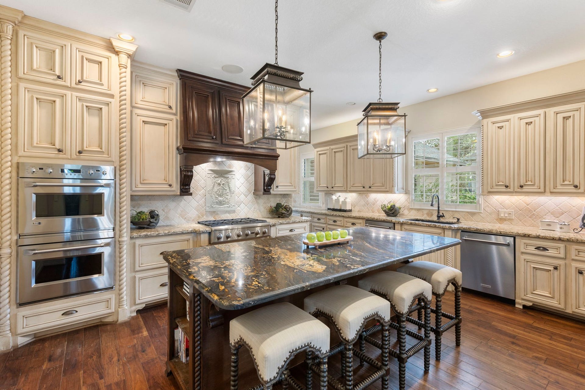 Chefs Kitchen showcasing exceptional craftsmanship with rich wood flooring and a striking accent island featuring high-end granite, built-in microwave, and lantern-style pendant lighting.
