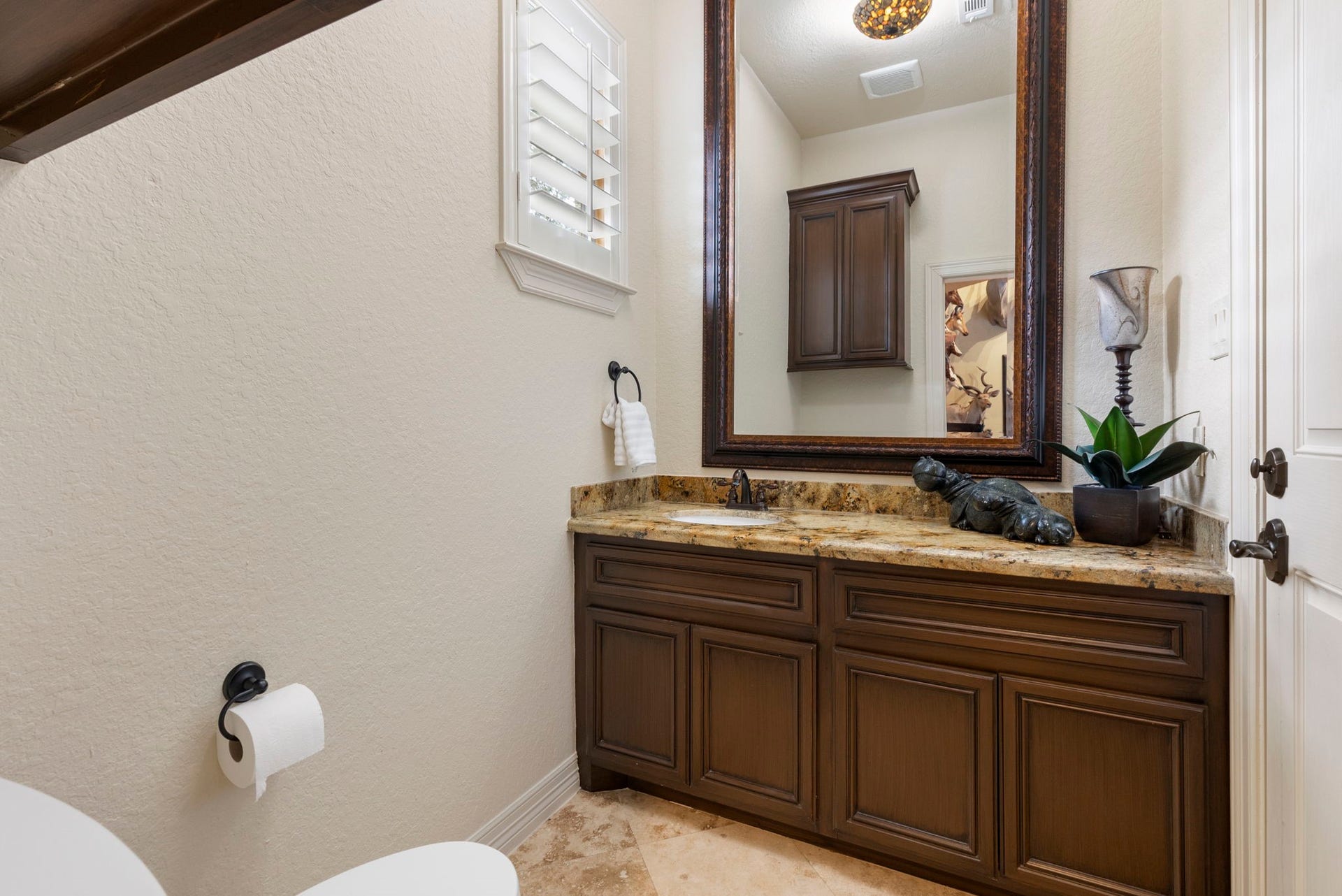 Convenient Game Lounge powder bath ideal for guests while entertaining, featuring Travertine flooring, granite vanity, and direct access to the backyard, pool area, and outdoor shower.