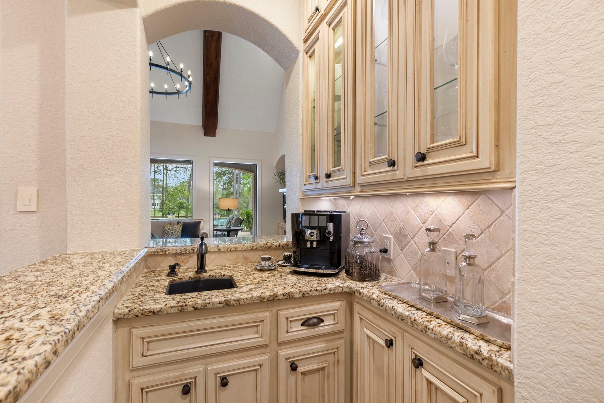 Dedicated coffee and wine serving bar with bar sink, granite countertops, glass-front cabinetry with accent lighting, and under-cabinet illuminationperfect for entertaining or morning coffee rituals.