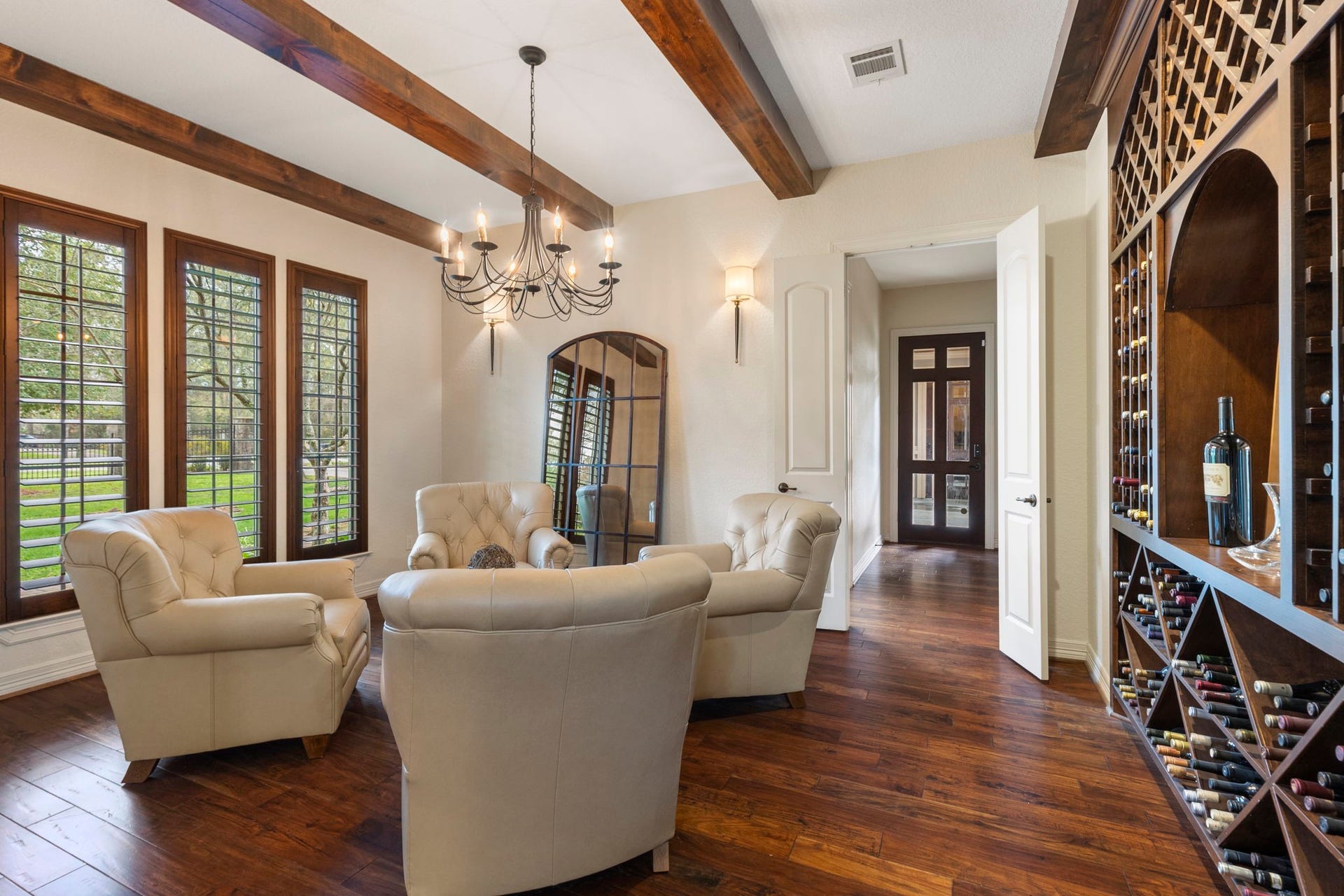 Elegant Formal Dining or Executive Lounge framed by an arched entry, rich wood flooring, and beam-accented ceiling. Tall shuttered windows, designer lighting, and wall sconces.