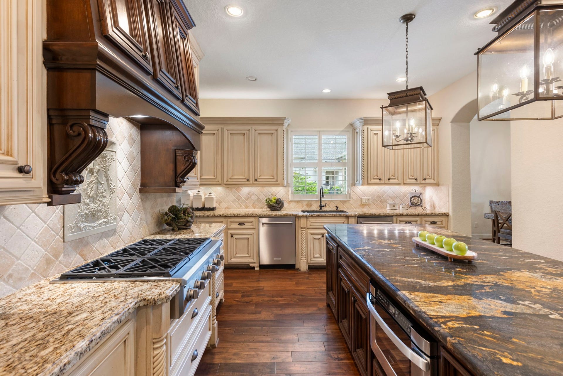 Custom vent hood anchors the Kitchen with a beautiful tumbled stone backsplash, under-cabinet and upper accent lighting, and a single-basin composite sink perfectly positioned beneath a window for natural light.