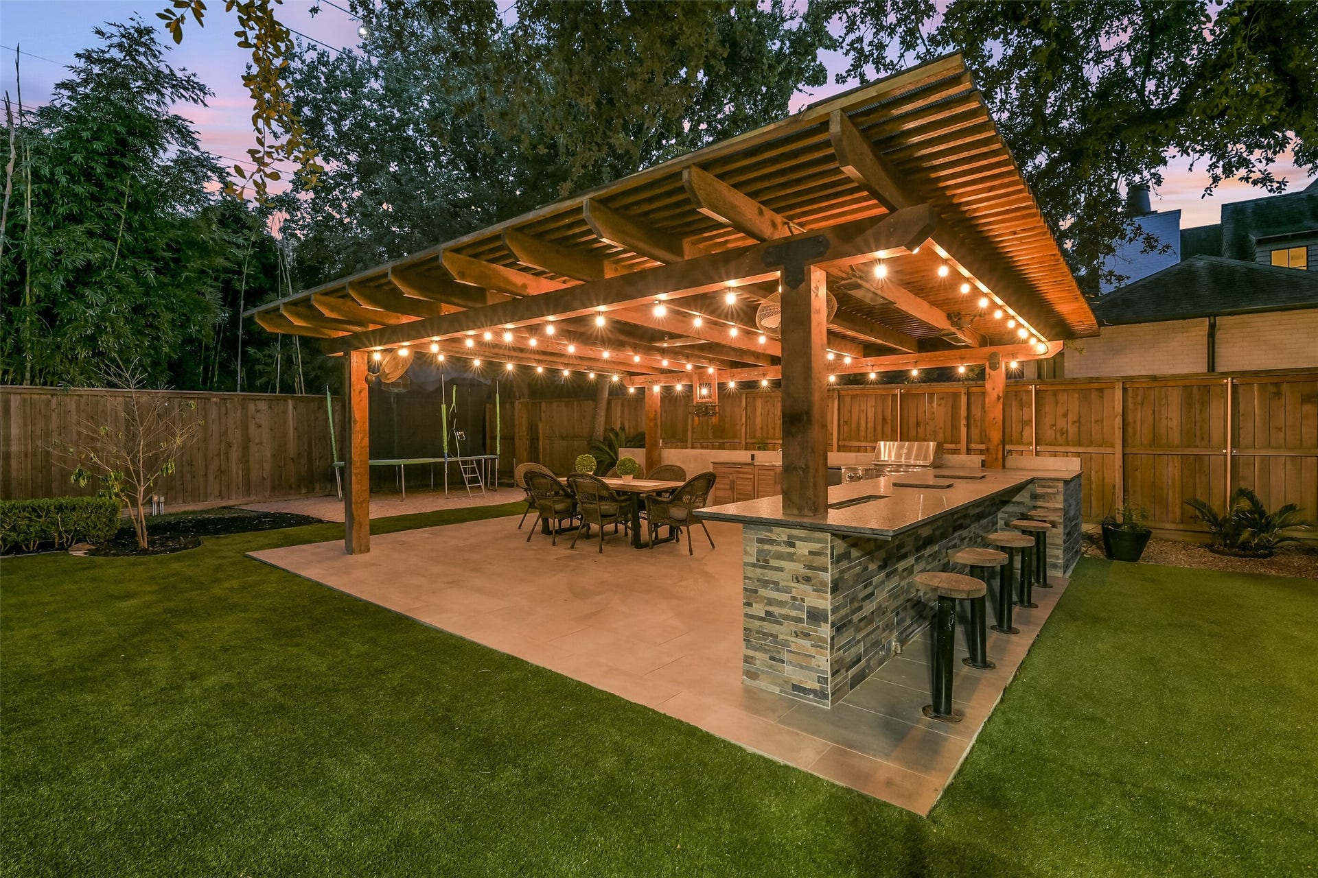 Another view of the fabulous outdoor entertaining area, featuring a spacious covered pavilion with a fully equipped outdoor kitchen, generous bar seating, and a dining area. Warm ambient lighting creates an inviting atmosphere, perfect for effortless entertaining and enjoying evenings with family and friends.