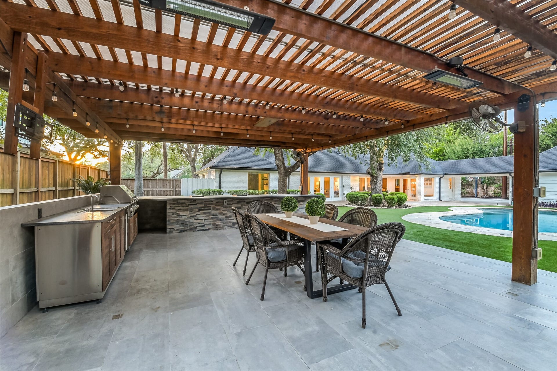 Impressive covered outdoor entertaining area featuring a spacious outdoor kitchen with stainless steel appliances, generous counter space, and dining area all overlooking the pool and backyard.