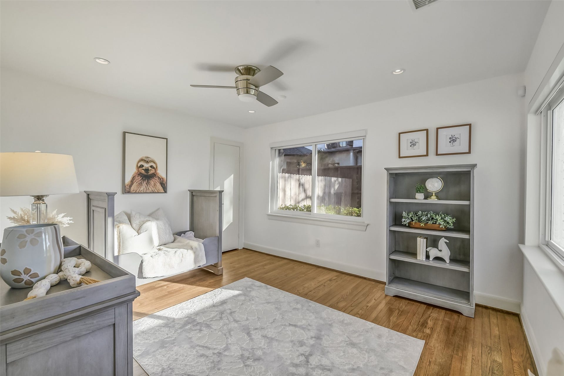 This versatile first-floor secondary bedroom, currently used as a nursery, featuring hardwood floors, recessed lighting, a ceiling fan, and large windows that fill the space with natural light. This inviting room could also serve beautifully as a private study or home office.