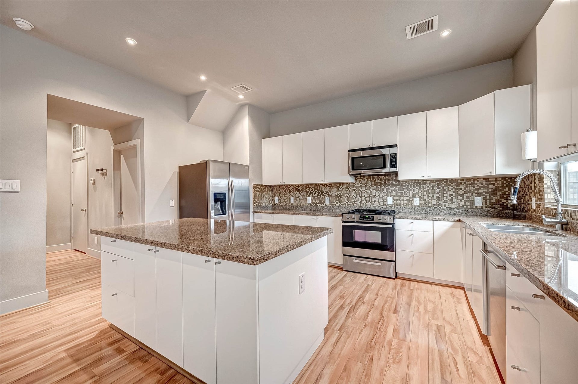 5111 Cornish Street, Houston, TX 77007 Spacious modern kitchen with sleek white cabinetry, granite countertops, stainless steel appliances, and a stylish mosaic backsplash.