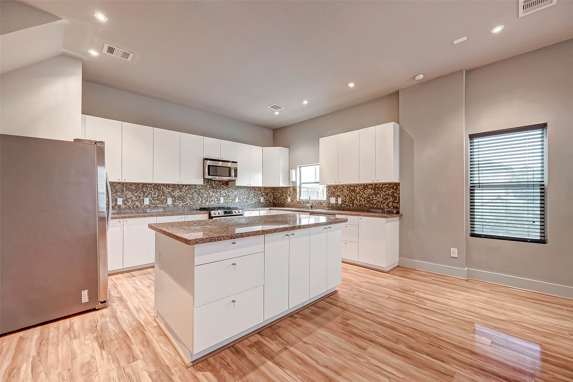 5111 Cornish Street, Houston, TX 77007 Modern kitchen with sleek white cabinetry, stainless steel appliances, and a stylish mosaic tile backsplash. A central island offers additional workspace, while the light wood flooring adds warmth to the space.