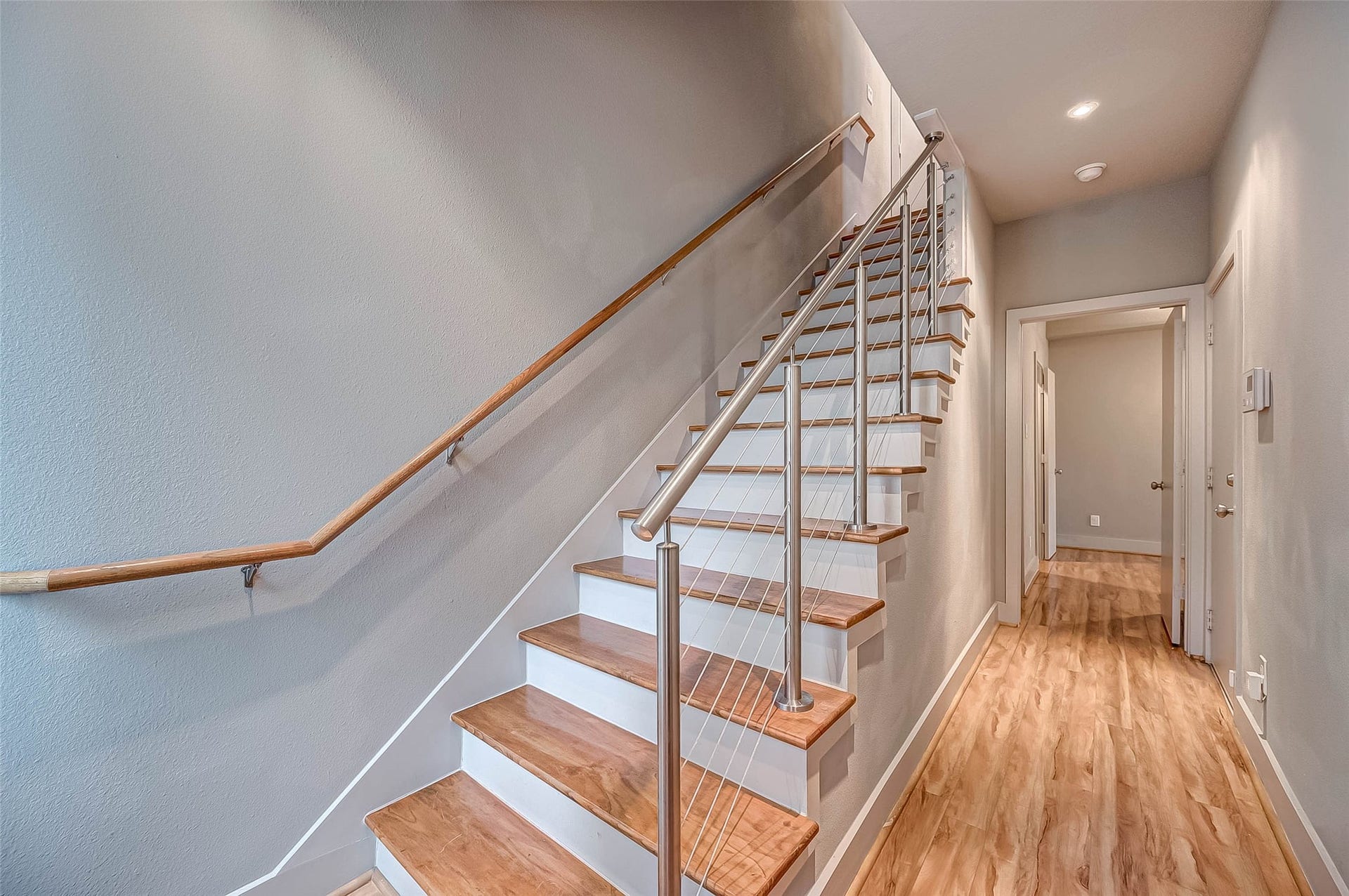 5111 Cornish Street, Houston, TX 77007 Modern staircase with sleek cable railing complements the bright, inviting hallway featuring warm wood flooring.