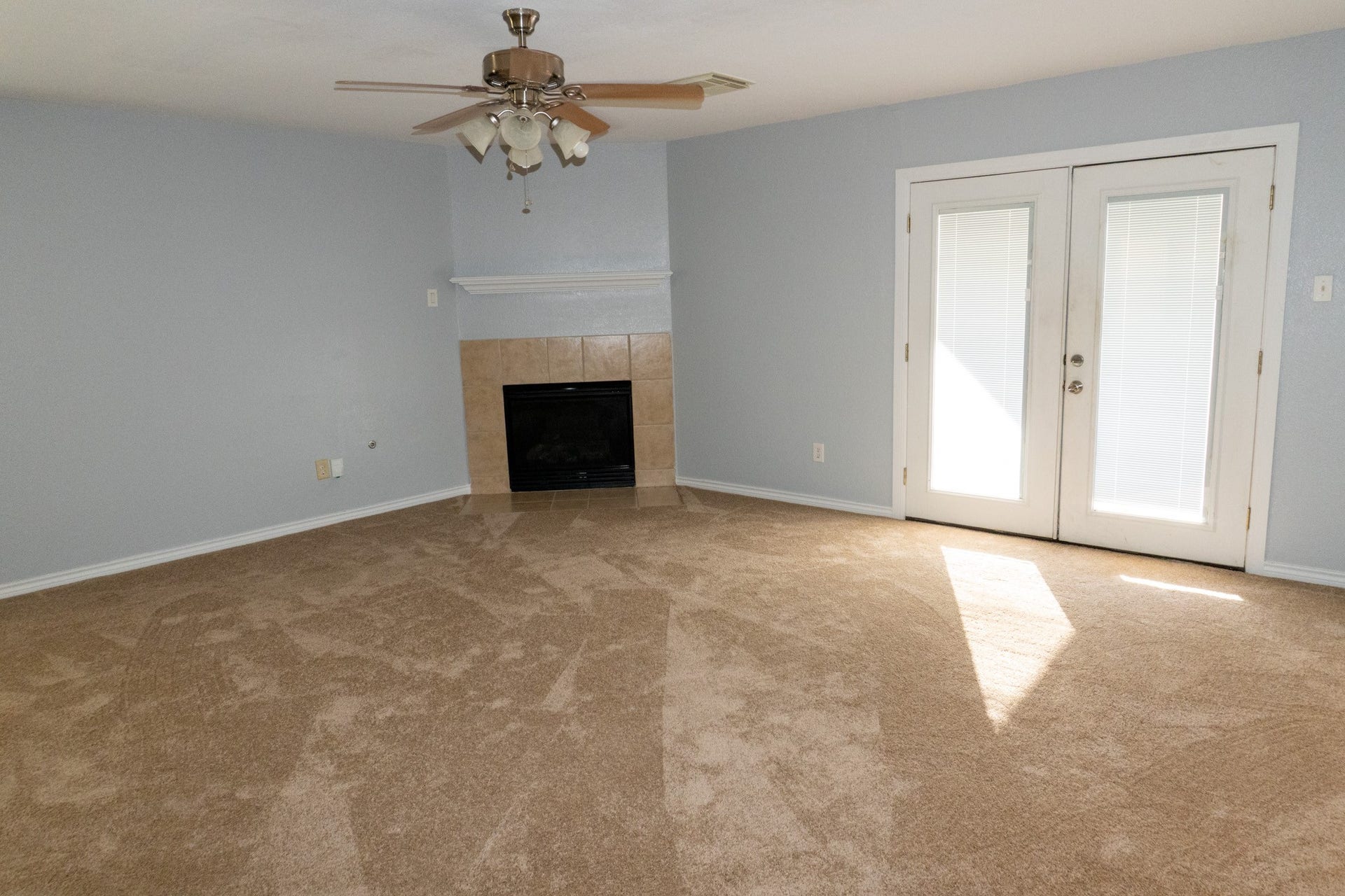 7627 Greenwood Point Drive, Cypress, TX 77433 Cozy living room featuring a warm carpet, elegant fireplace, and abundant natural light through French doors, complemented by a stylish ceiling fan.