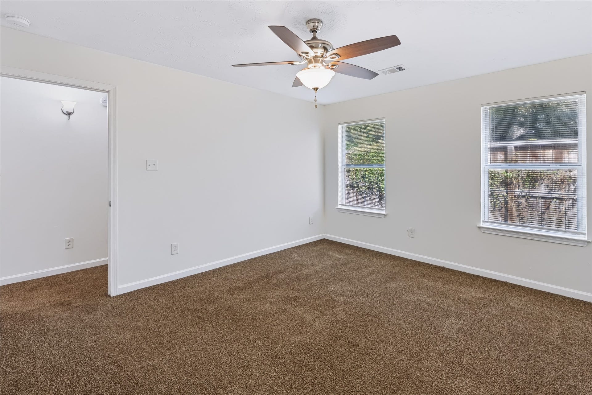 6528 Utah Street, Houston, TX 77091 Spacious room with neutral walls and carpet, illuminated by natural light from two windows and highlighted by a modern ceiling fan.