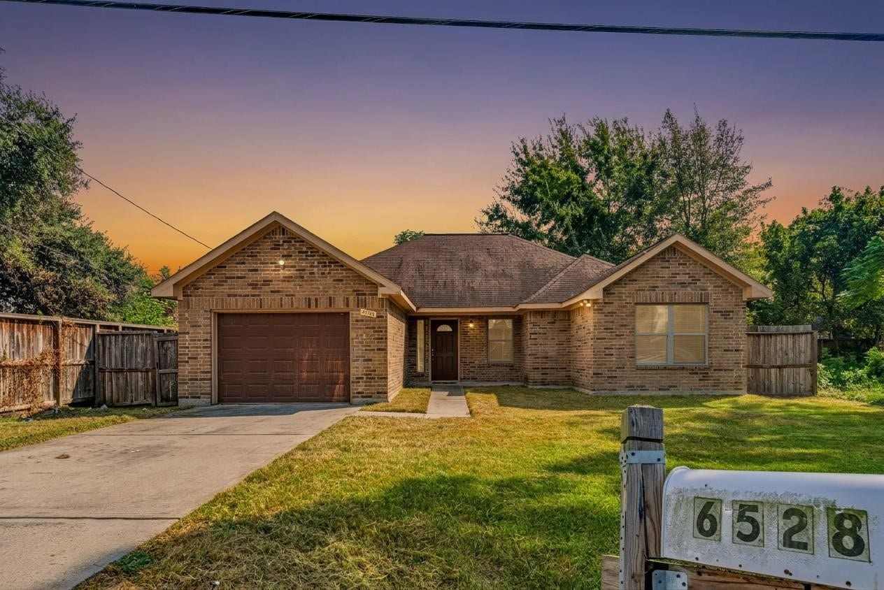 6528 Utah Street, Houston, TX 77091 Charming brick home with a welcoming front yard, single-car garage, and a cozy porch set against a picturesque sunset backdrop.
