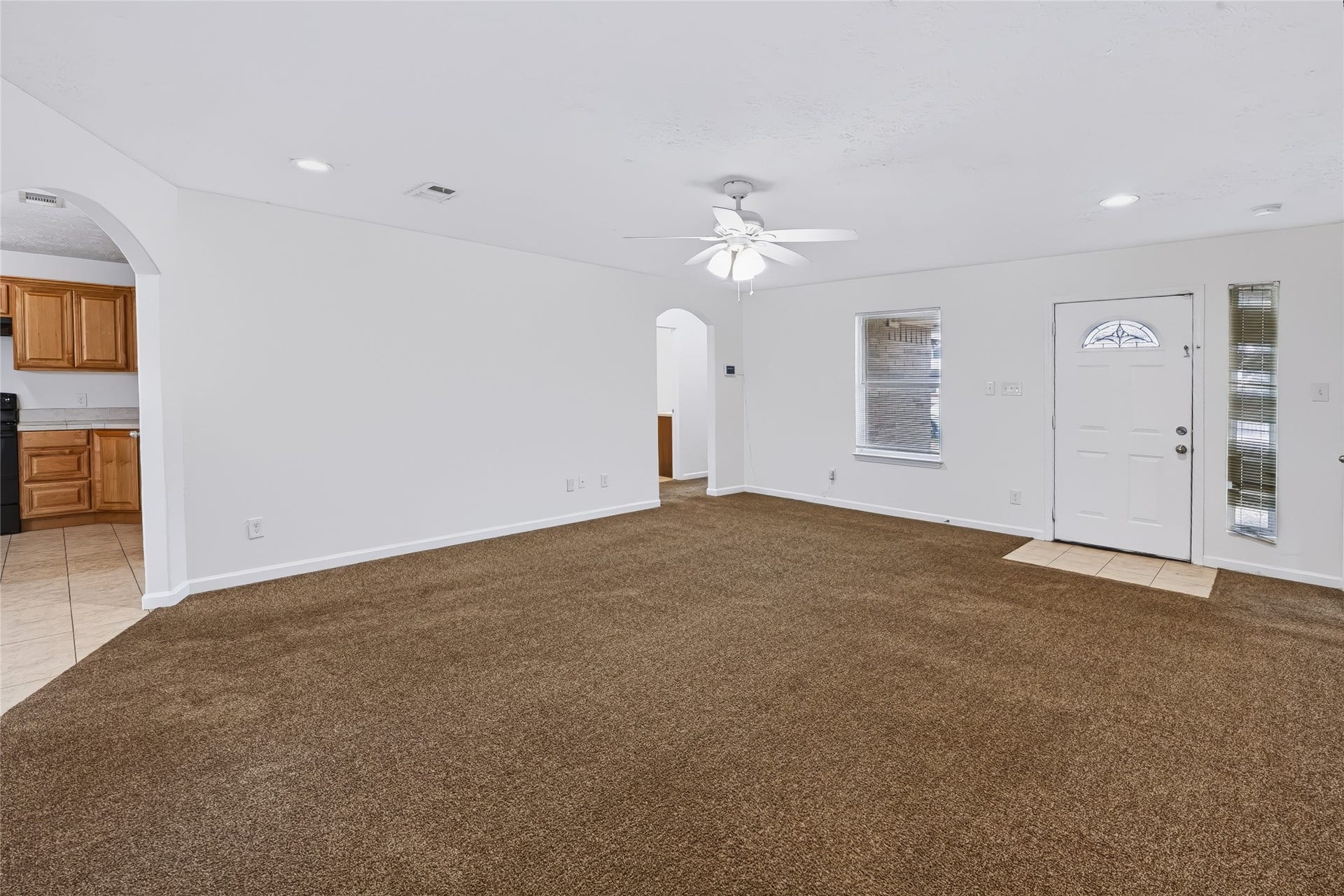 6528 Utah Street, Houston, TX 77091 Spacious living area with plush carpet and a ceiling fan, featuring a bright, open layout leading to the kitchen with wood cabinetry.