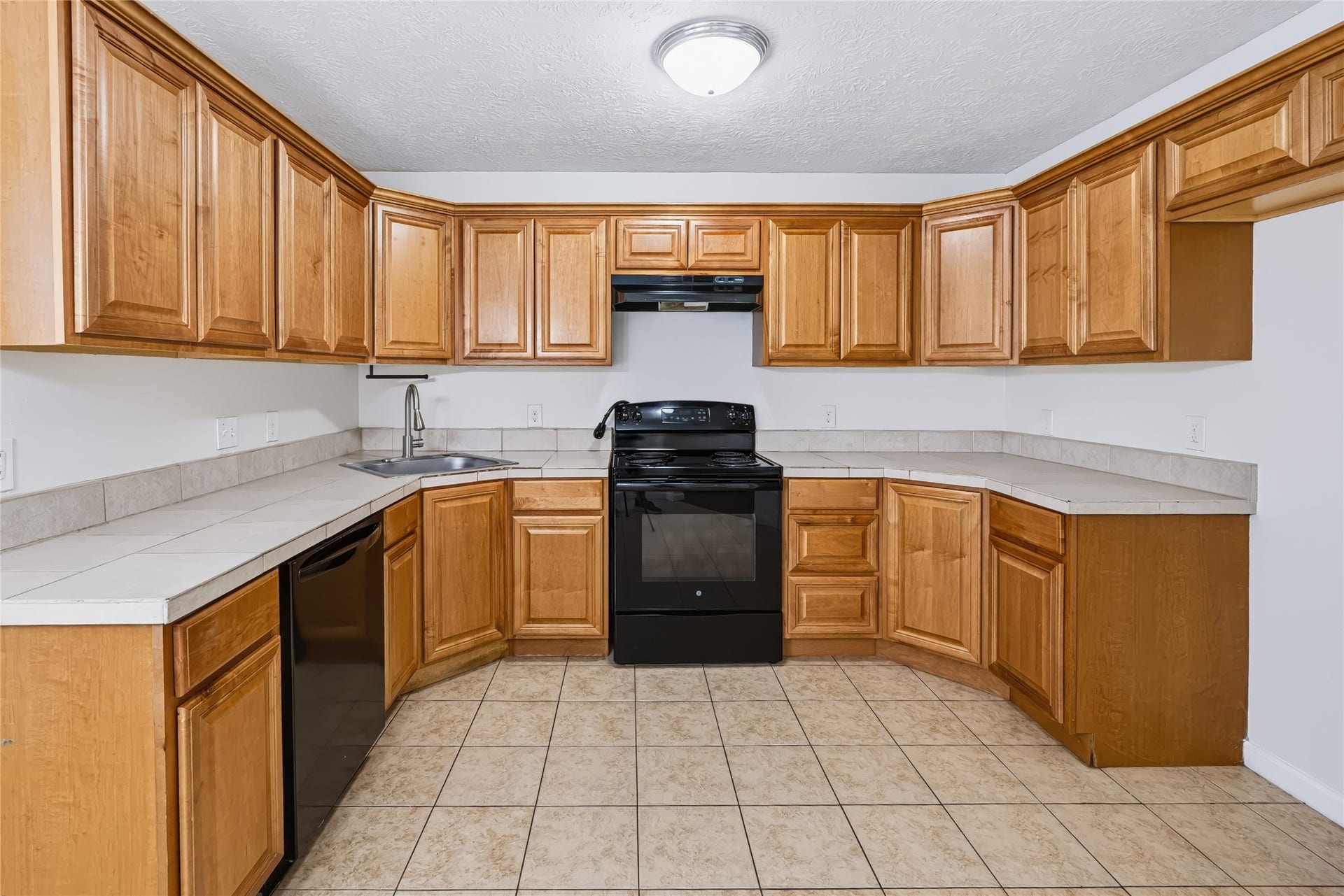 6528 Utah Street, Houston, TX 77091 Bright kitchen featuring ample wooden cabinetry, sleek black appliances, and a spacious tile floor, perfect for culinary endeavors.