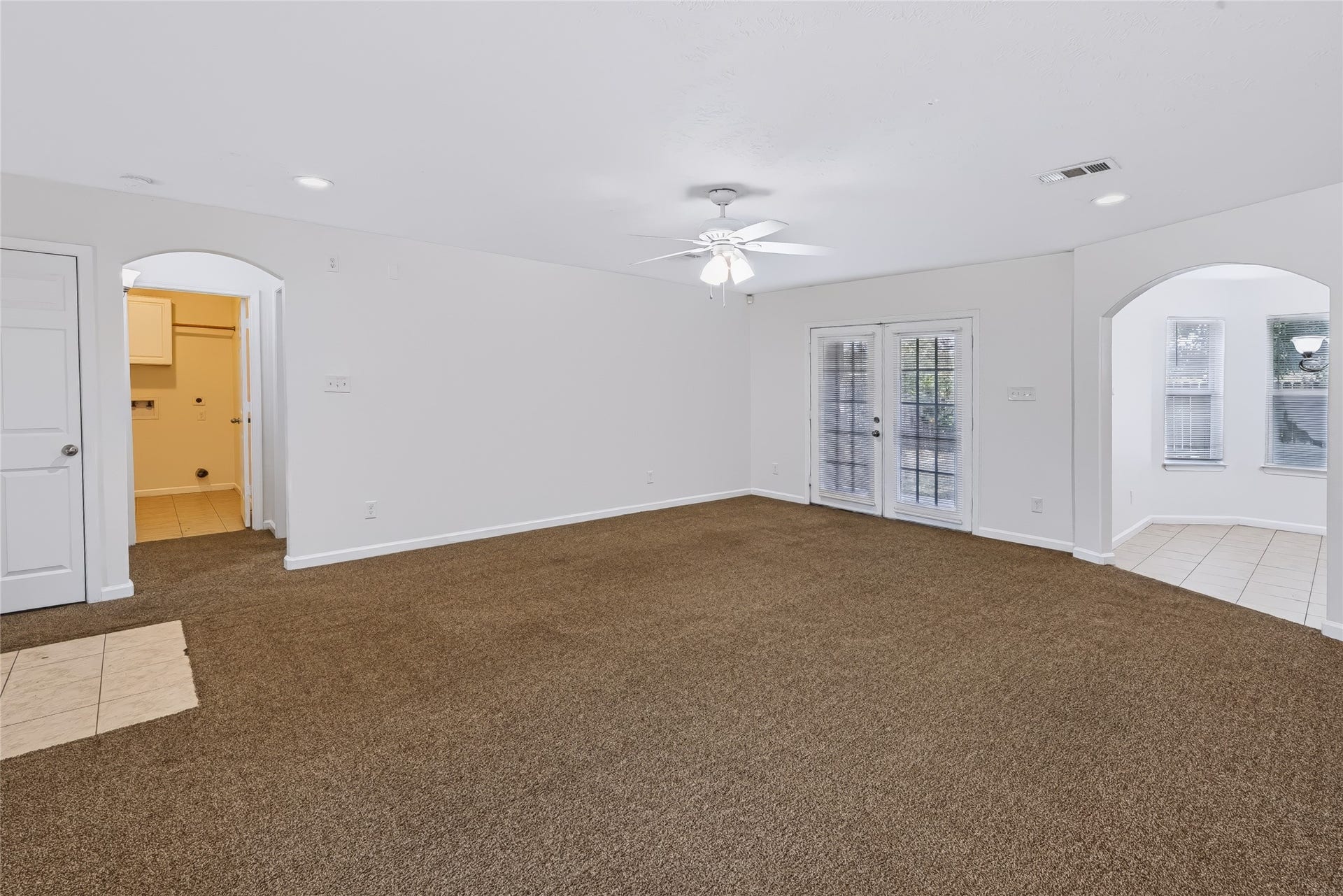 6528 Utah Street, Houston, TX 77091 Spacious living area with plush carpeting, ceiling fan, and natural light streaming through double glass doors, leading to a cozy adjacent tile-floored space.