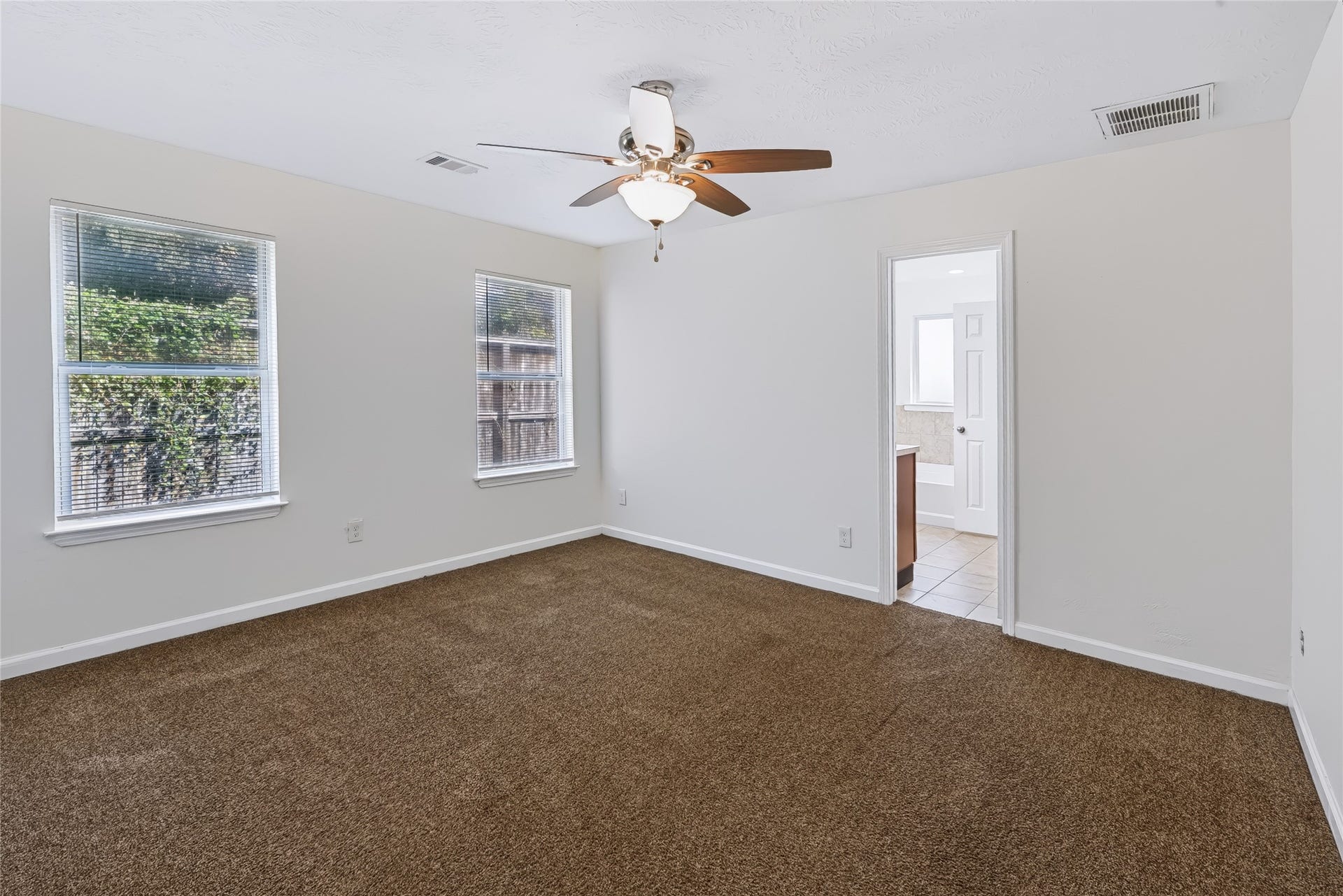 6528 Utah Street, Houston, TX 77091 Spacious bedroom with plush carpeting, abundant natural light from dual windows, and an attached bathroom for convenience.