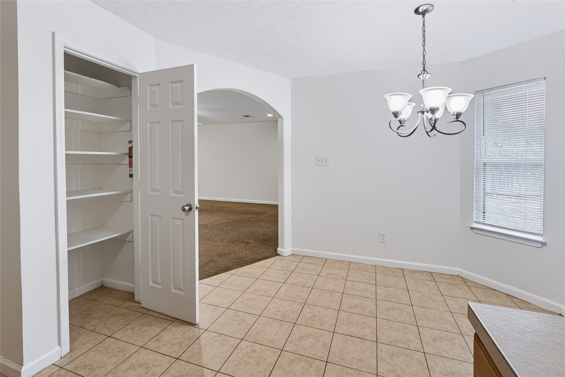 6528 Utah Street, Houston, TX 77091 Bright dining area with tiled flooring, a charming chandelier, and an open pantry. An archway connects to the cozy carpeted living space.