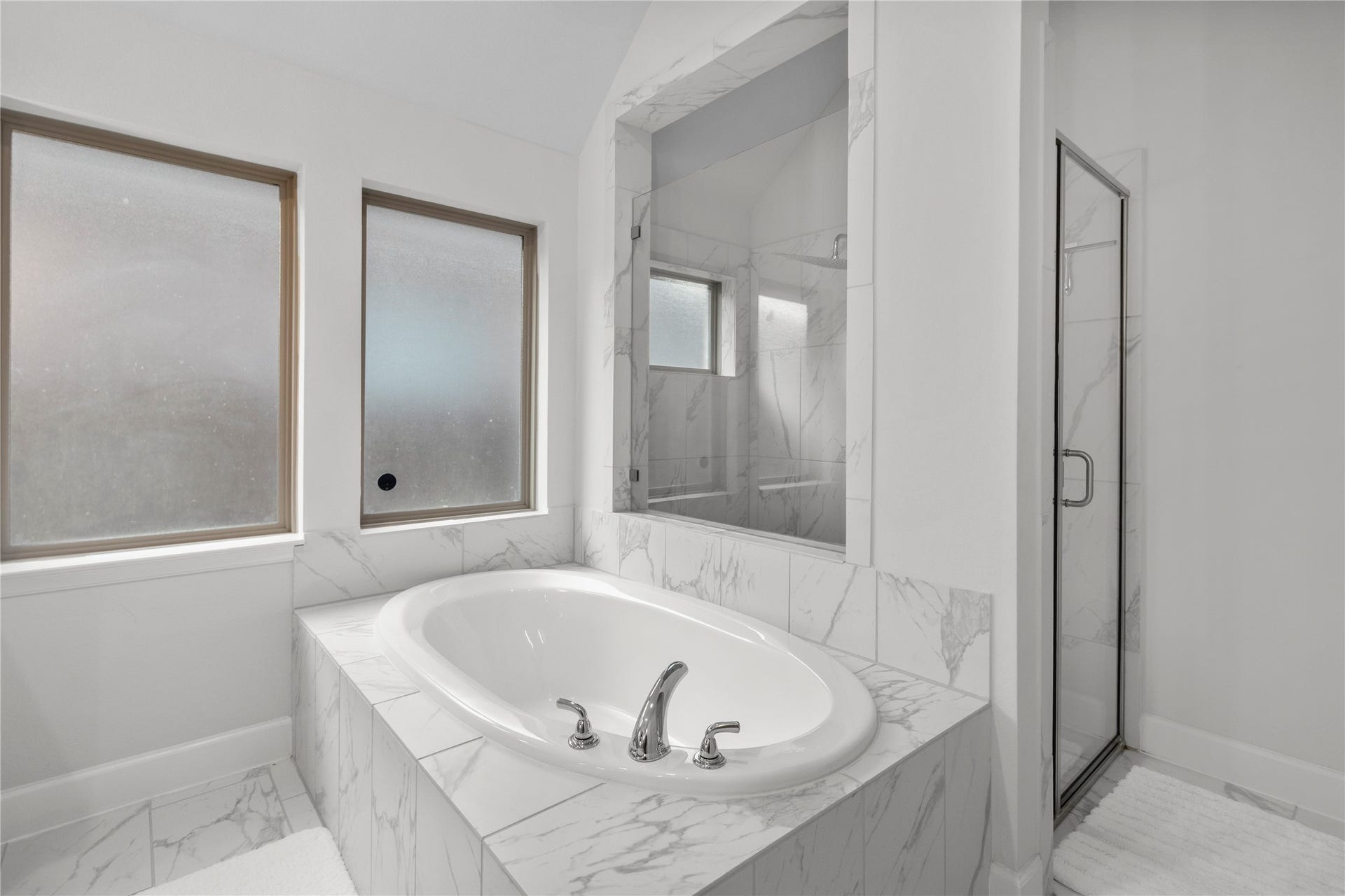 9934 Starry Night Lane, Manvel, TX 77578 Elegant bathroom featuring a luxurious marble-tiled soaking tub and a spacious glass-enclosed shower, complemented by frosted windows for privacy and natural light.