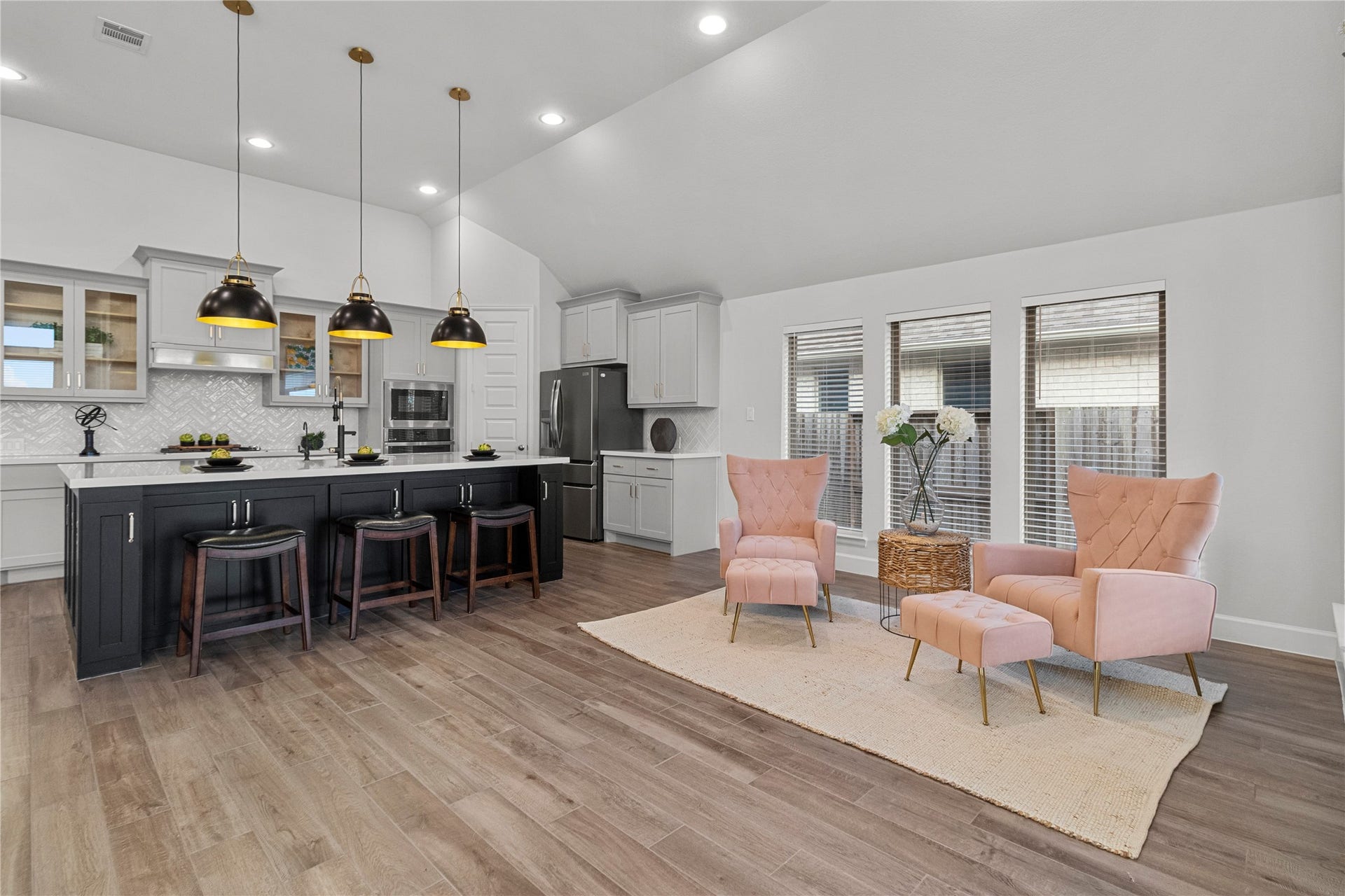 9934 Starry Night Lane, Manvel, TX 77578 A modern open-concept living area features a sleek kitchen with a large island, pendant lighting, and ample seating. The space seamlessly flows into a cozy sitting area with plush pink chairs and abundant natural light.