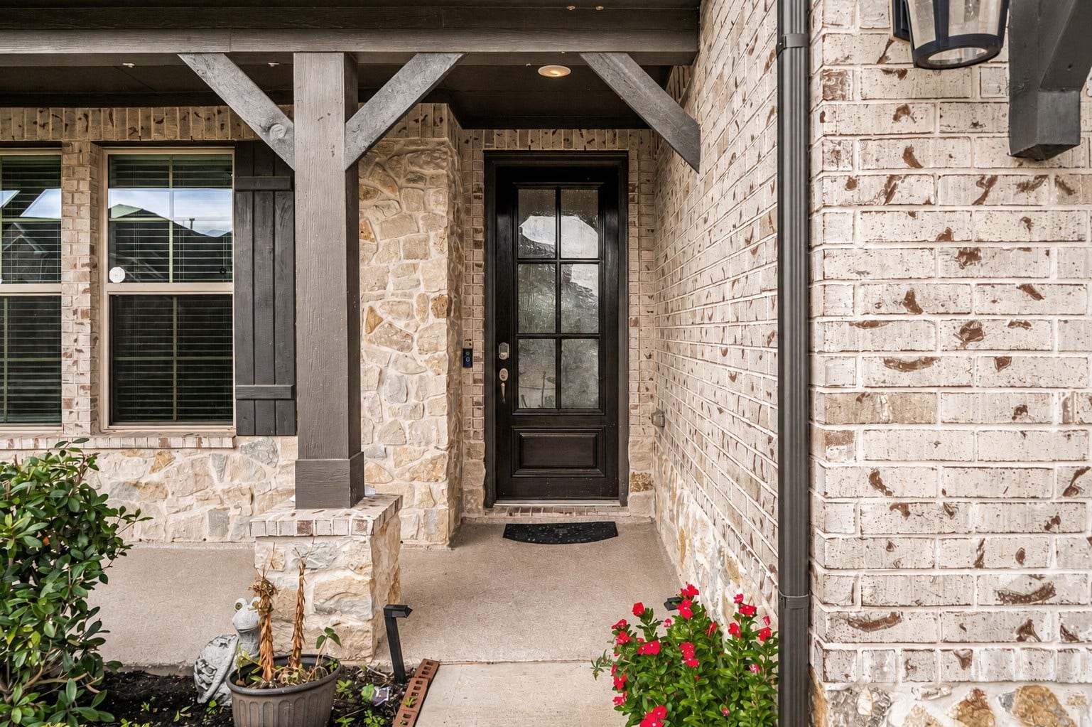 31619 Donoso Drive, Fulshear, TX 77441 A covered front porch with upgraded flooring welcomes guests home, accented by decorative beams and vibrant entry landscaping.