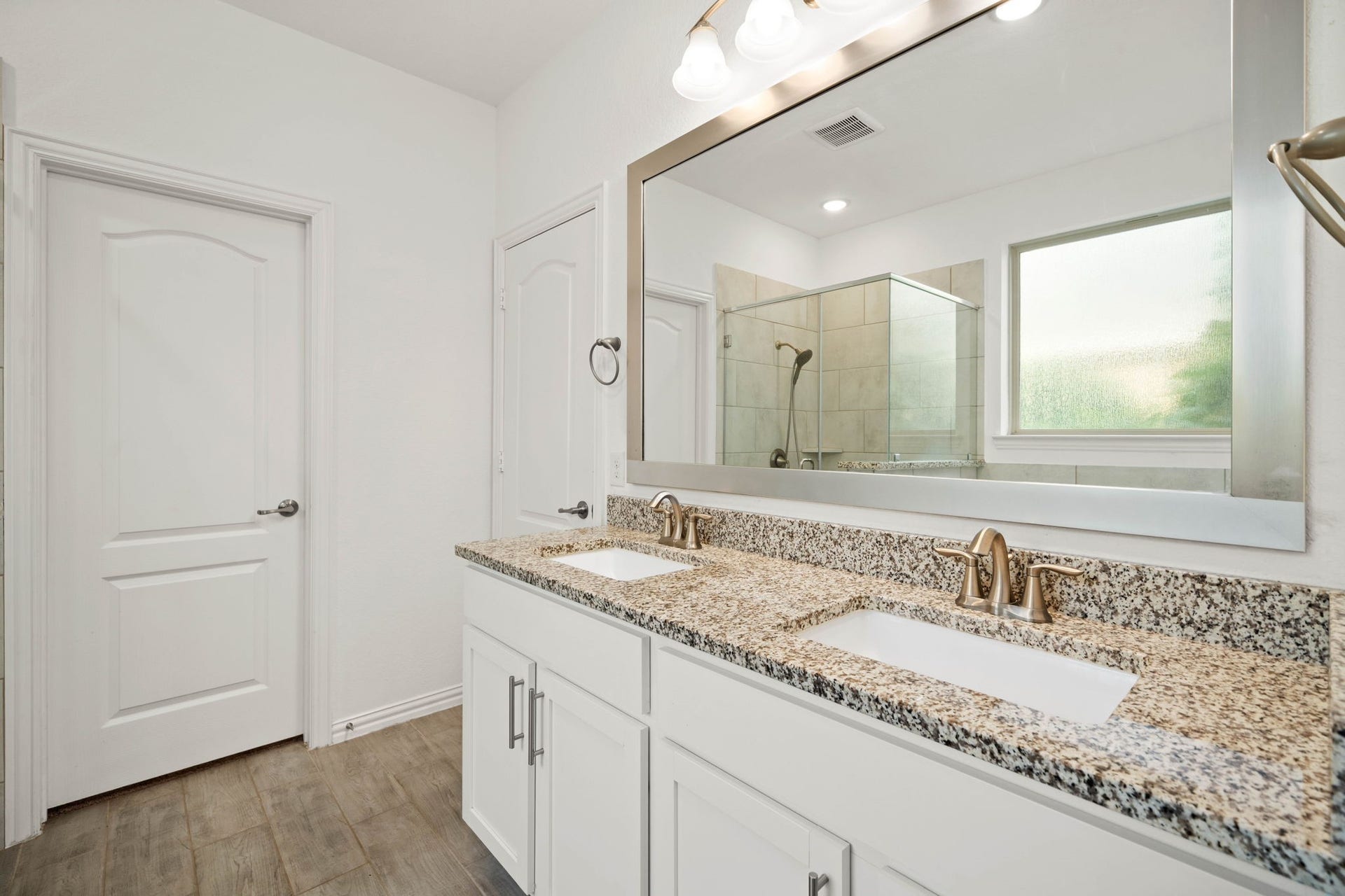31619 Donoso Drive, Fulshear, TX 77441 The primary bath offers a granite-topped double vanity with a framed mirror and ample cabinet storage, with a glimpse of the separate walk-in shower beyond.