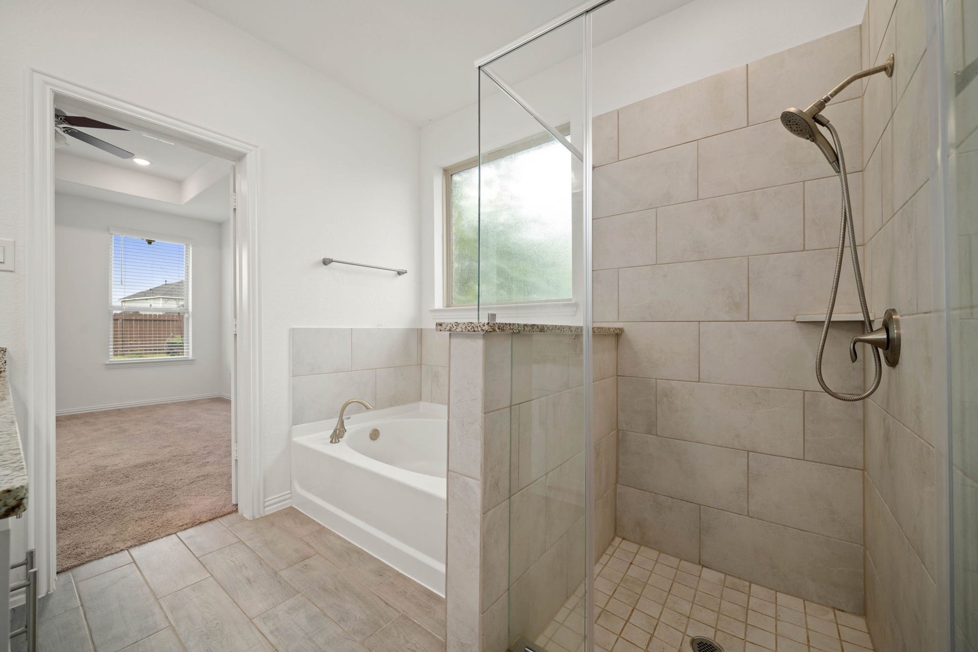 31619 Donoso Drive, Fulshear, TX 77441 A soaking tub and separate walk-in shower with tile surround create a spa-like retreat in the primary bath, filled with natural light from the frosted window.