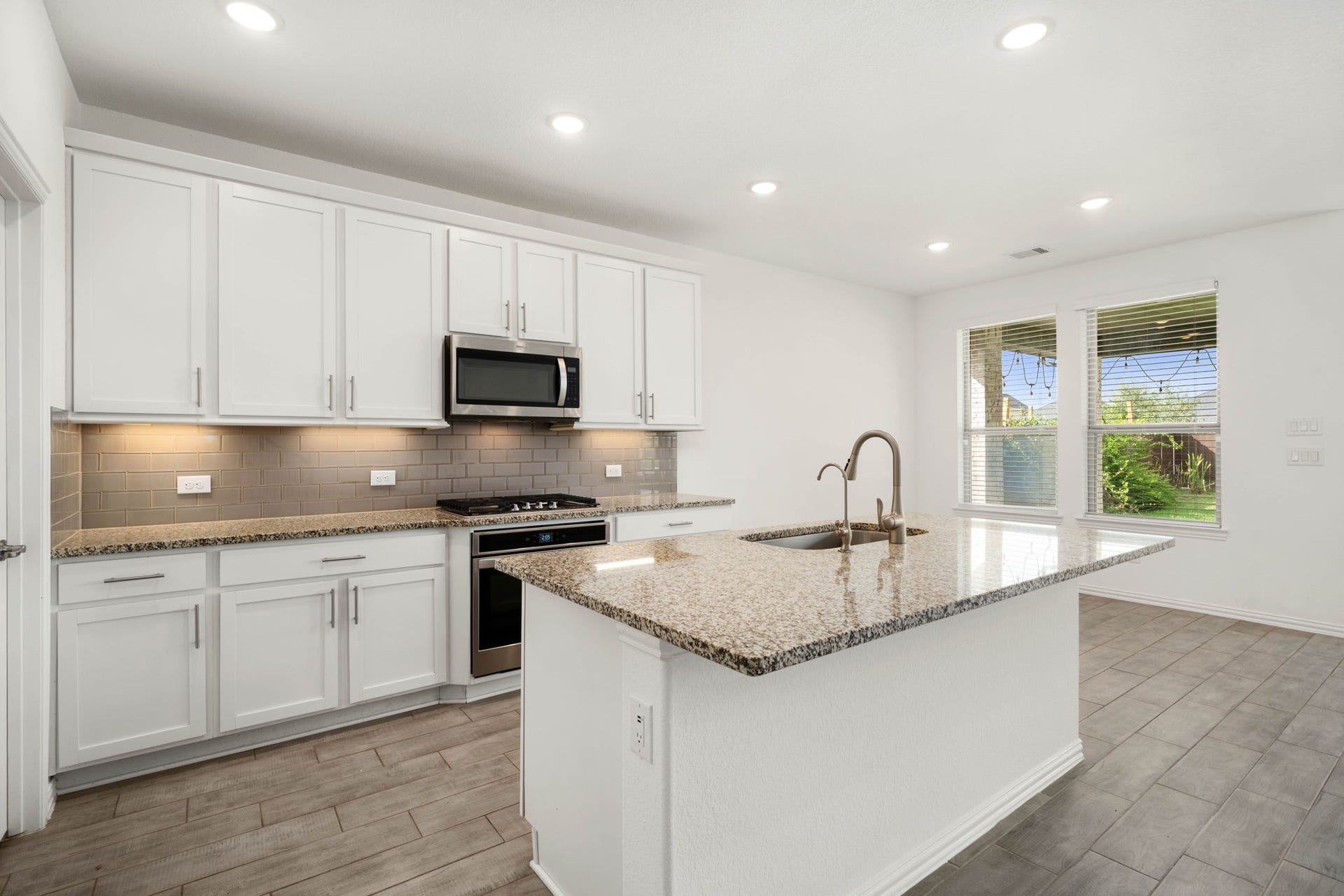 31619 Donoso Drive, Fulshear, TX 77441 A gas cooktop and tile backsplash add style and function to the kitchen, with under-cabinet lighting and a window overlooking the backyard.