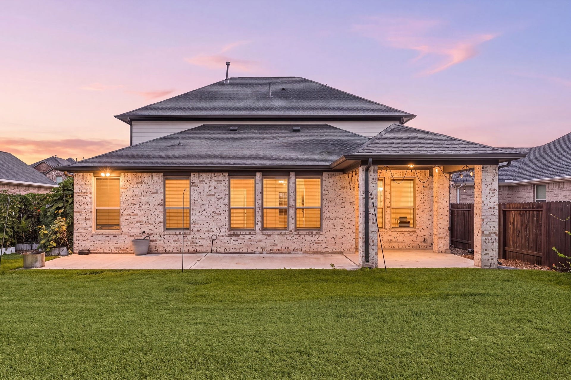 31619 Donoso Drive, Fulshear, TX 77441 As evening falls, the extended concrete patio, spanning the full width of the home offers a covered seating area highlighted by string lights, perfect for relaxing outdoors.
