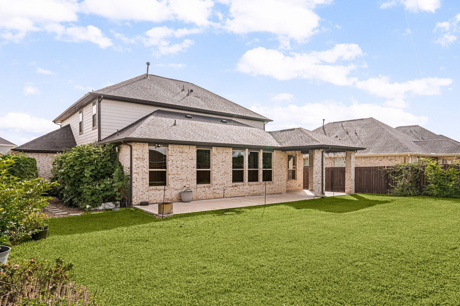 31619 Donoso Drive, Fulshear, TX 77441 In daylight, the same extended patio showcases the home's full-width concrete space alongside lush, flowering vines along the side yard.