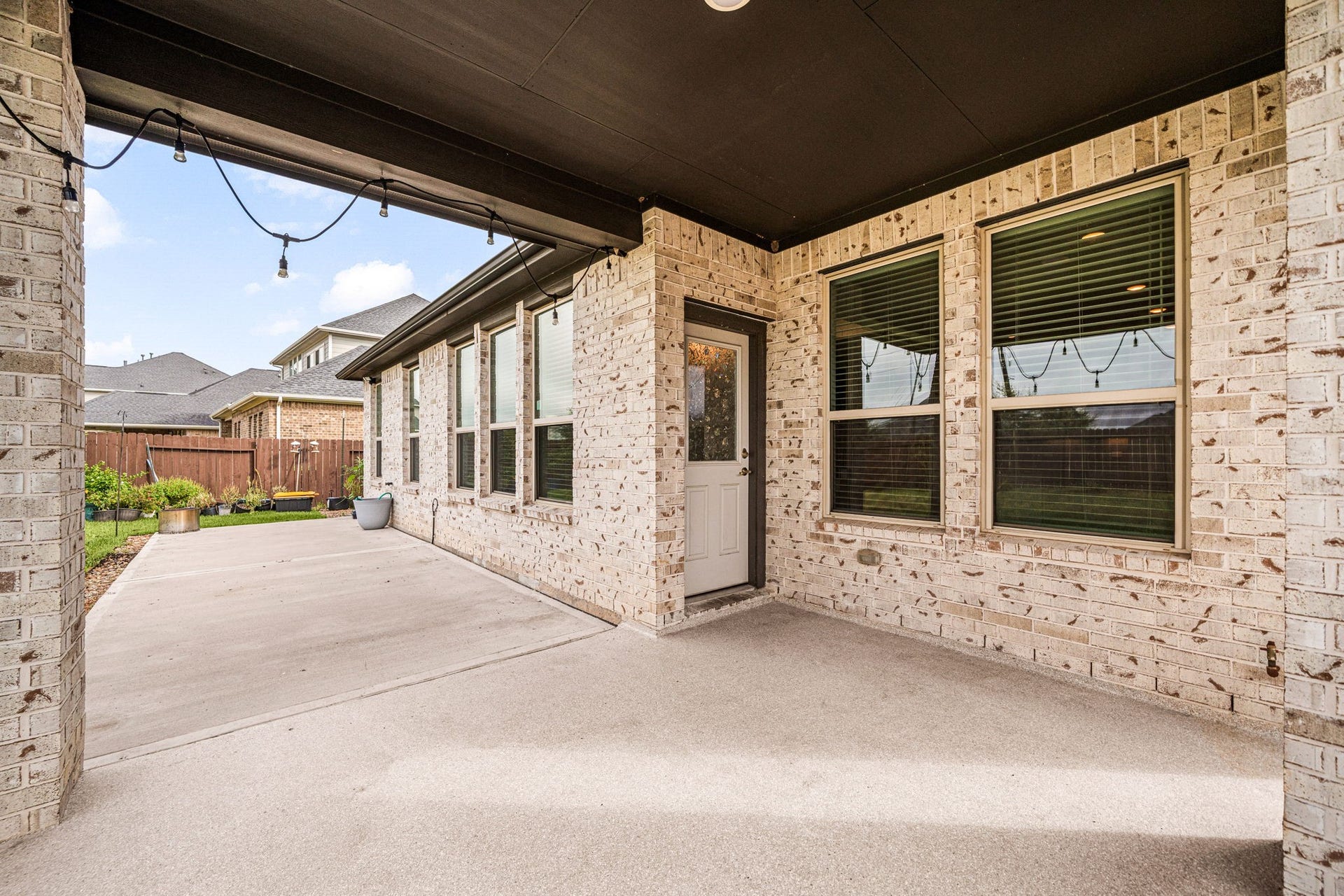 31619 Donoso Drive, Fulshear, TX 77441 The covered patio provides a shaded outdoor living space with access to the home, complete with charming string lighting for evening ambiance.