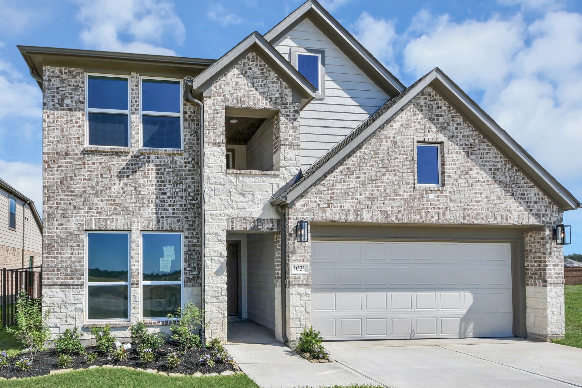 1021 Golden Glow Path, Magnolia, TX 77355 Meticulously maintained yard and lush landscape, paired with a premium elevation featuring captivating brick accents. Modern coach lights add a touch of contemporary elegance to the exterior.