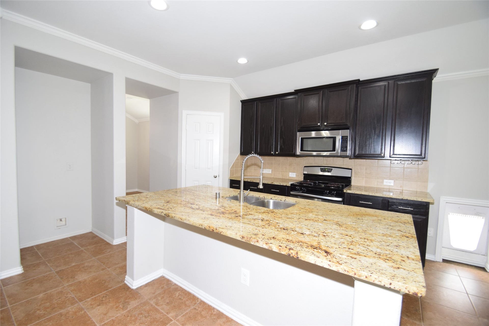 Kitchen offering tile floors, granite counter tops, island with sink and breakfast bar, tile back splash, gas cooking, built-in microwave and a walk-in pantry.
