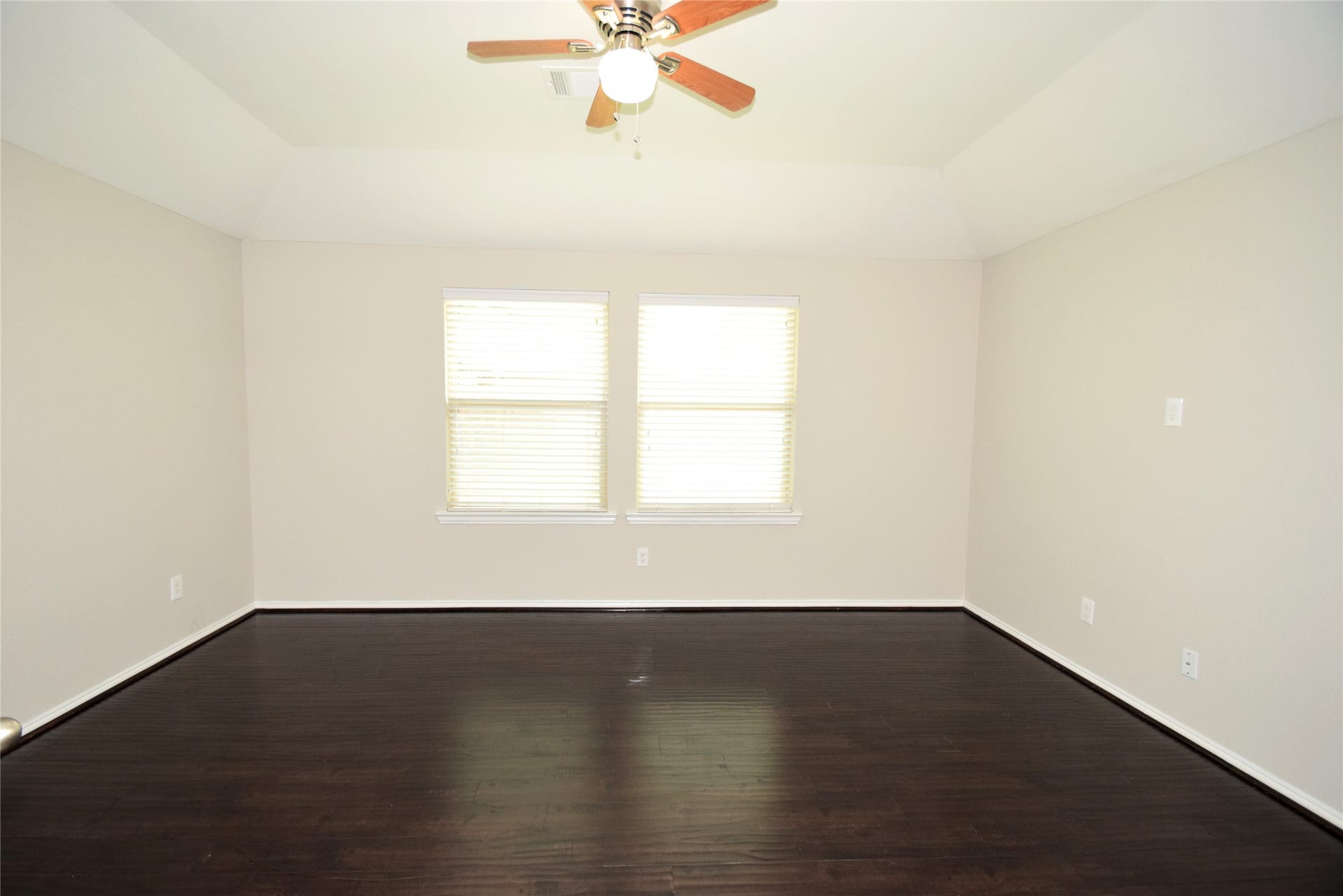 Primary bedroom complimented by hardwood floors, raised ceilings and a ceiling fan with light fixture.