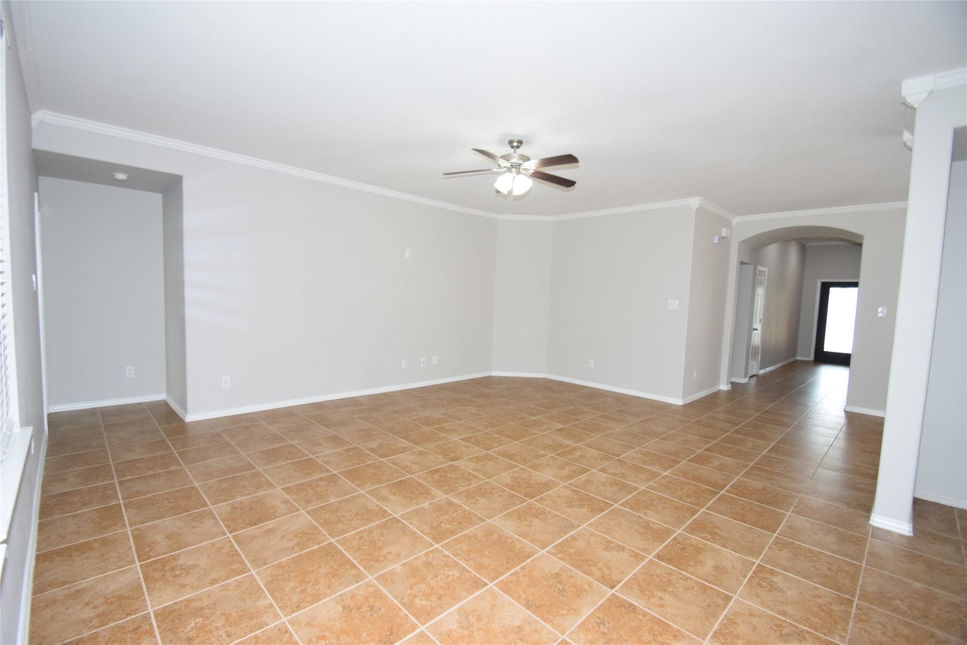 Spacious family room featuring tile floors, crown molding, ceiling fan with light fixture and open to the kitchen.