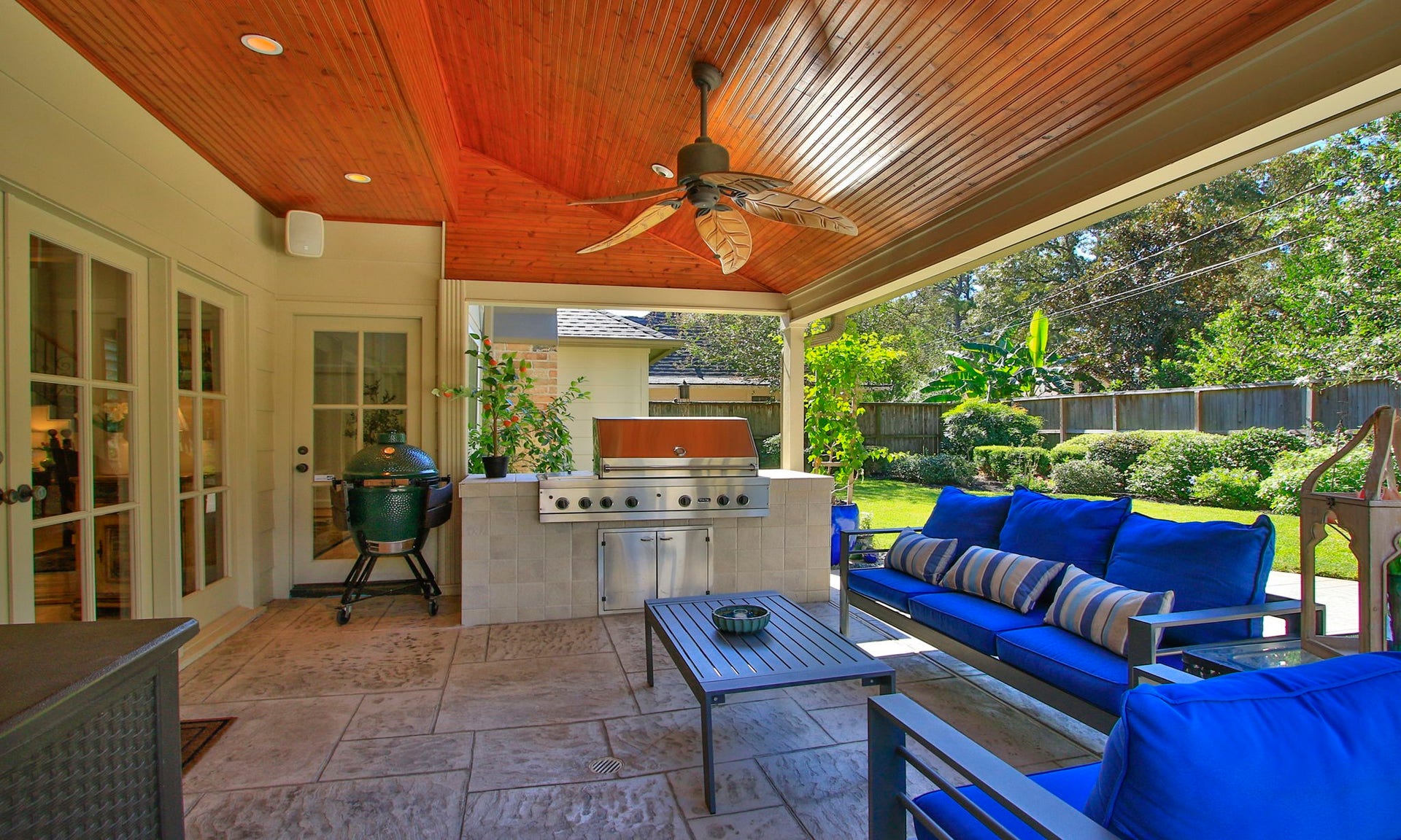 16131 Rudgewick Lane, Spring, TX 77379 Experience outdoor living at its finest with this beautifully designed patio featuring a built-in grill, and a ceiling fan under a warm wood-paneled ceiling, all set against a lush garden backdrop.