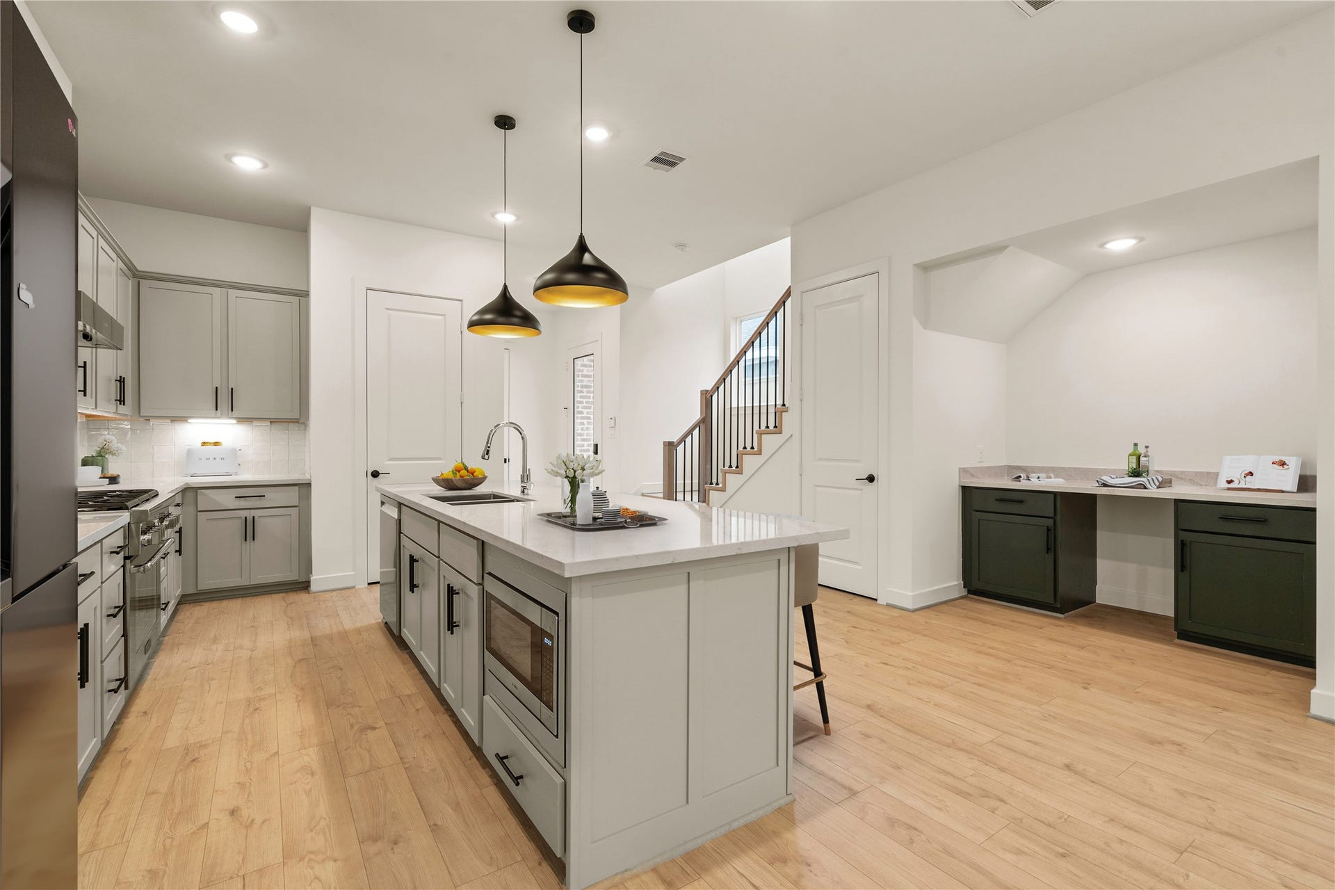 5018 Schuler Street, Houston, TX 77007 Gourmet kitchen and bar area spacious quartz-topped island with under-cabinet microwave, matte black pendant lights, soft-grey shaker cabinetry, and an adjacent wet bar nook set over light oak flooring.