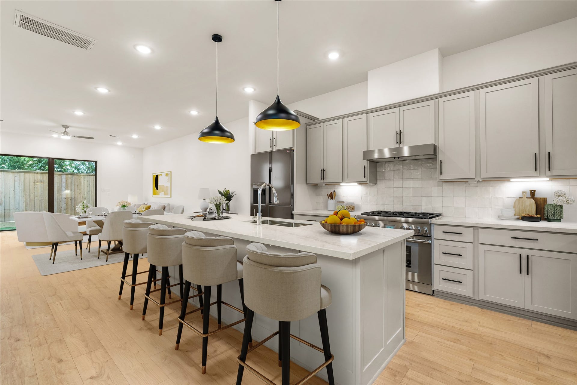 5018 Schuler Street, Houston, TX 77007 Chef-inspired kitchen design large prep island featuring elegant bar seating, gas range with stainless vent hood, crisp zellige tile backsplash, and open flow toward the light-filled dining space.