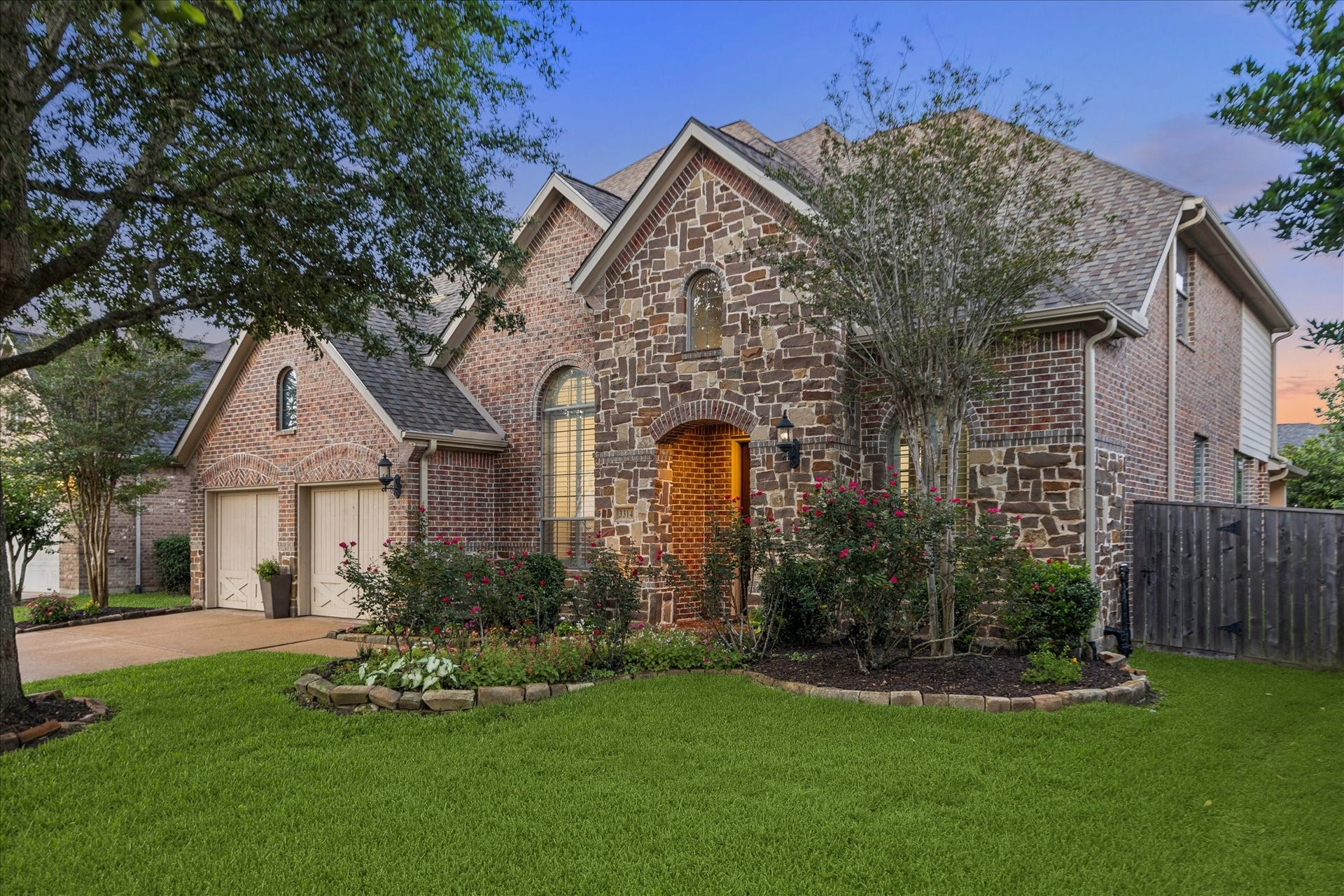 3314 Ravens Roost, Missouri City, TX 77459 The storybook curb appeal starts right here with a beautiful brick and stone exterior, arched entry, lush lawn, mature trees, colorful landscaping, and a 3-car garage tucked to the side. From the charming architectural details to the inviting front approach, this home makes a memorable first impression before you even step inside.