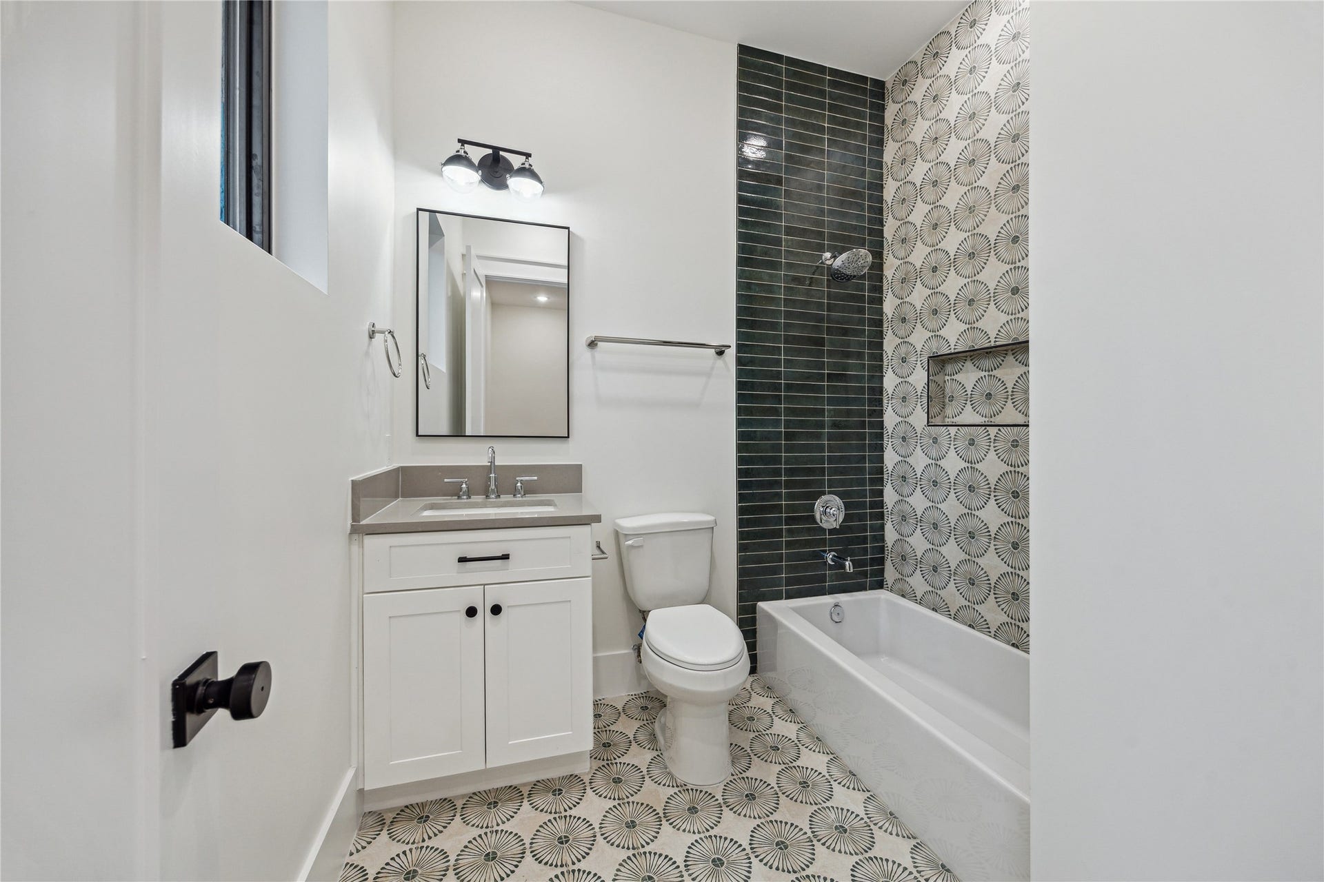 431 W 30th Street, Houston, TX 77018 This bathroom features modern design with a white vanity, sleek black fixtures, and a bathtub with stylish geometric tile accents. The space is bright, thanks to natural light from the window, and offers a clean, contemporary look.
