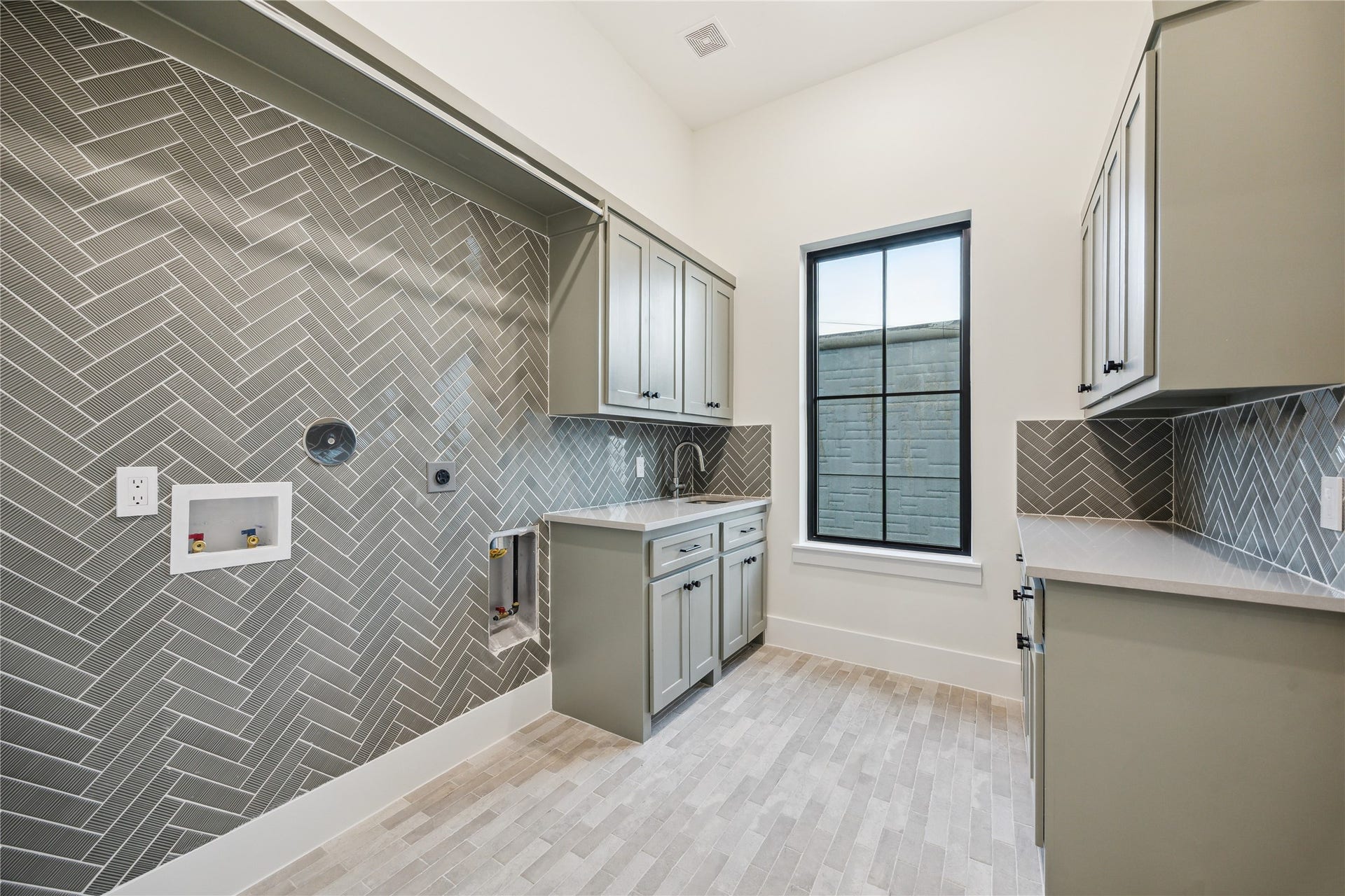431 W 30th Street, Houston, TX 77018 This modern downstairs laundry room features herringbone-patterned tile walls, ample cabinetry, and a large window for natural light. It's designed for functionality and style, with a sleek and organized layout.