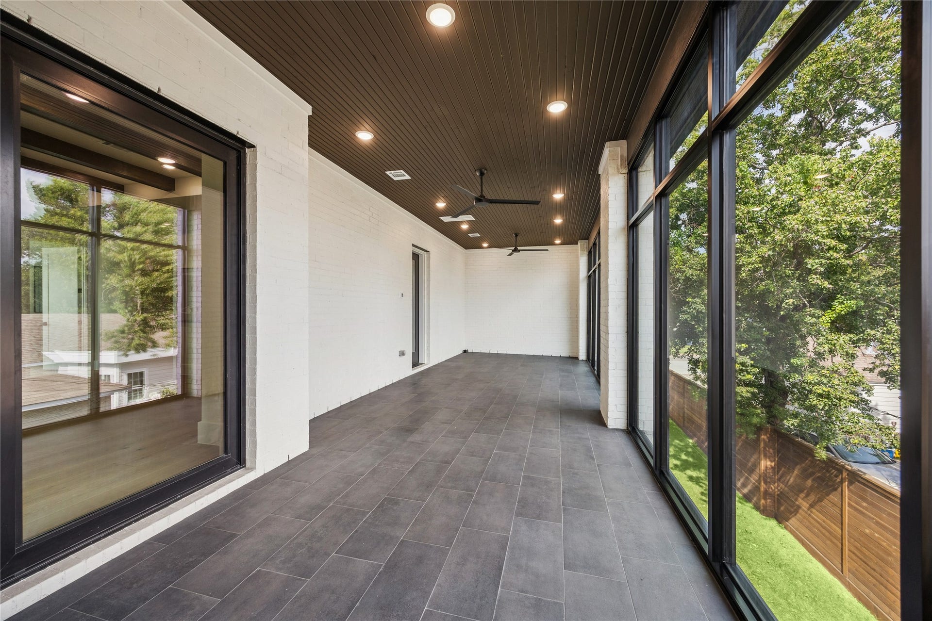 431 W 30th Street, Houston, TX 77018 This photo shows a spacious enclosed patio with large windows offering abundant natural light and views of greenery. It features a sleek, dark tiled floor and ceiling fans, creating a comfortable environment for relaxation or entertaining.