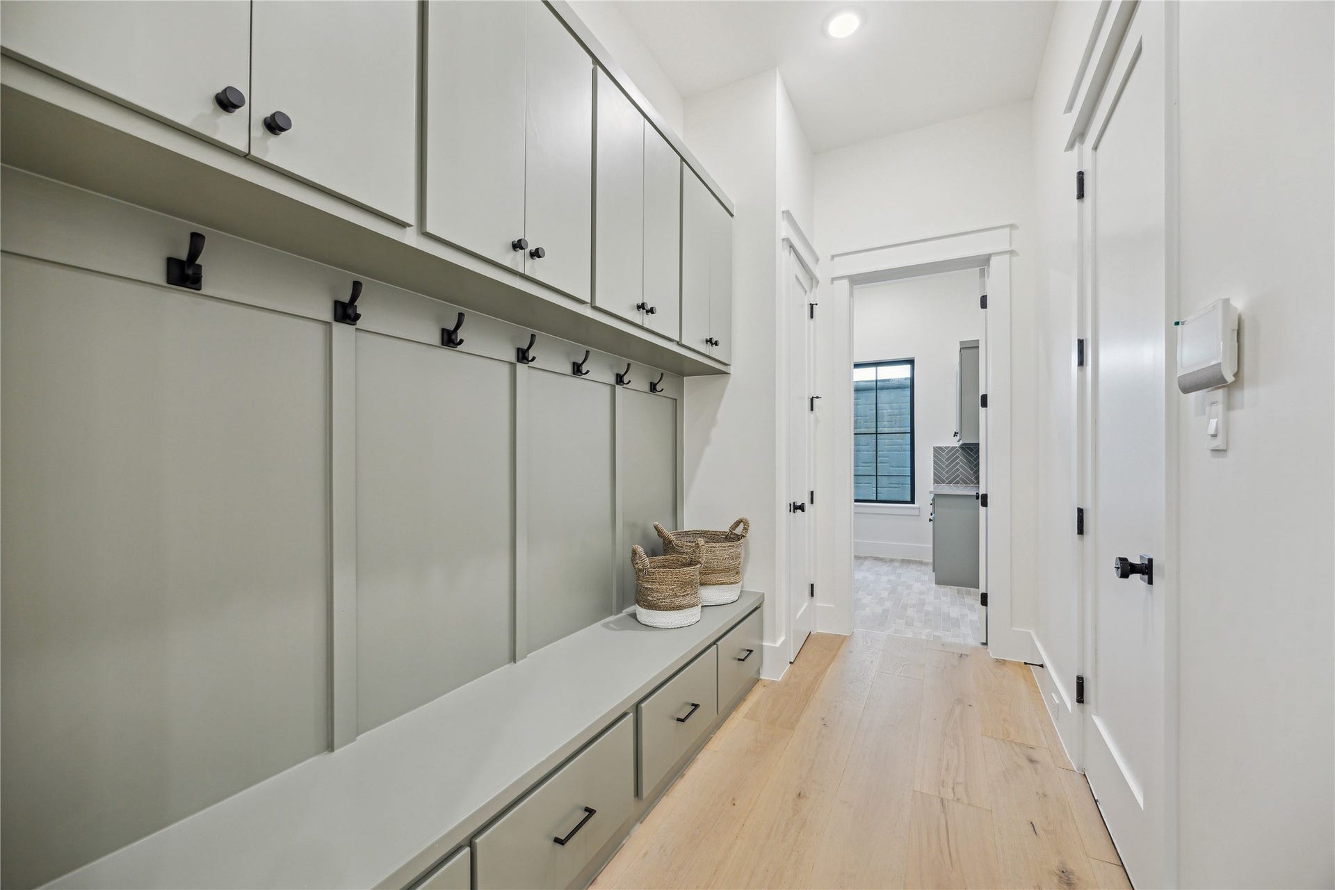 431 W 30th Street, Houston, TX 77018 This photo showcases a bright, modern mudroom with ample built-in storage, a bench with drawers, and coat hooks. The light wood flooring complements the sleek cabinetry, and a doorway leads to an adjacent room.