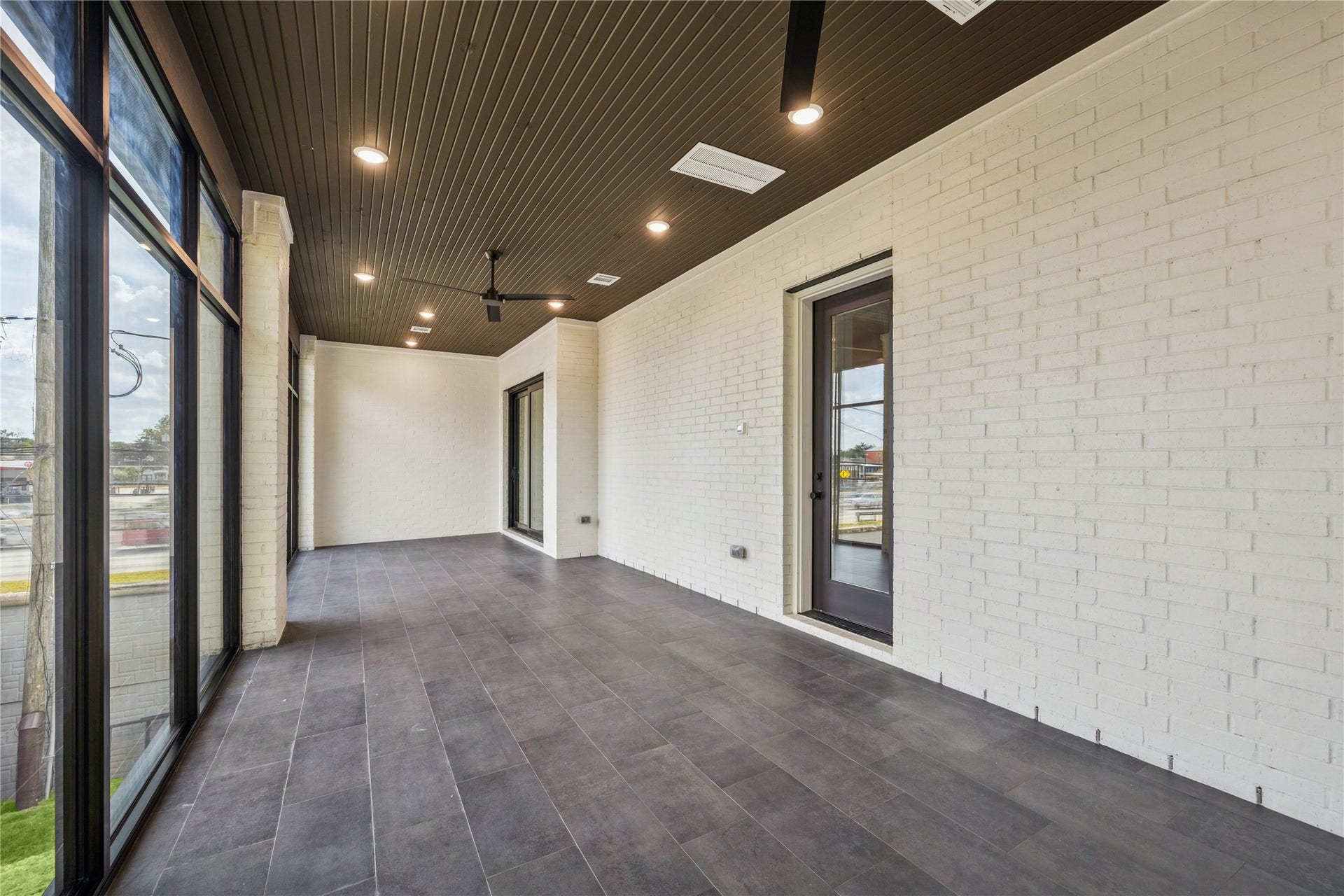 431 W 30th Street, Houston, TX 77018 This photo showcases a spacious, enclosed patio with large windows, providing ample natural light. It features modern dark floor tiles, a wood-paneled ceiling with recessed lighting, and ceiling fans, offering a stylish and comfortable space for relaxation or entertaining.