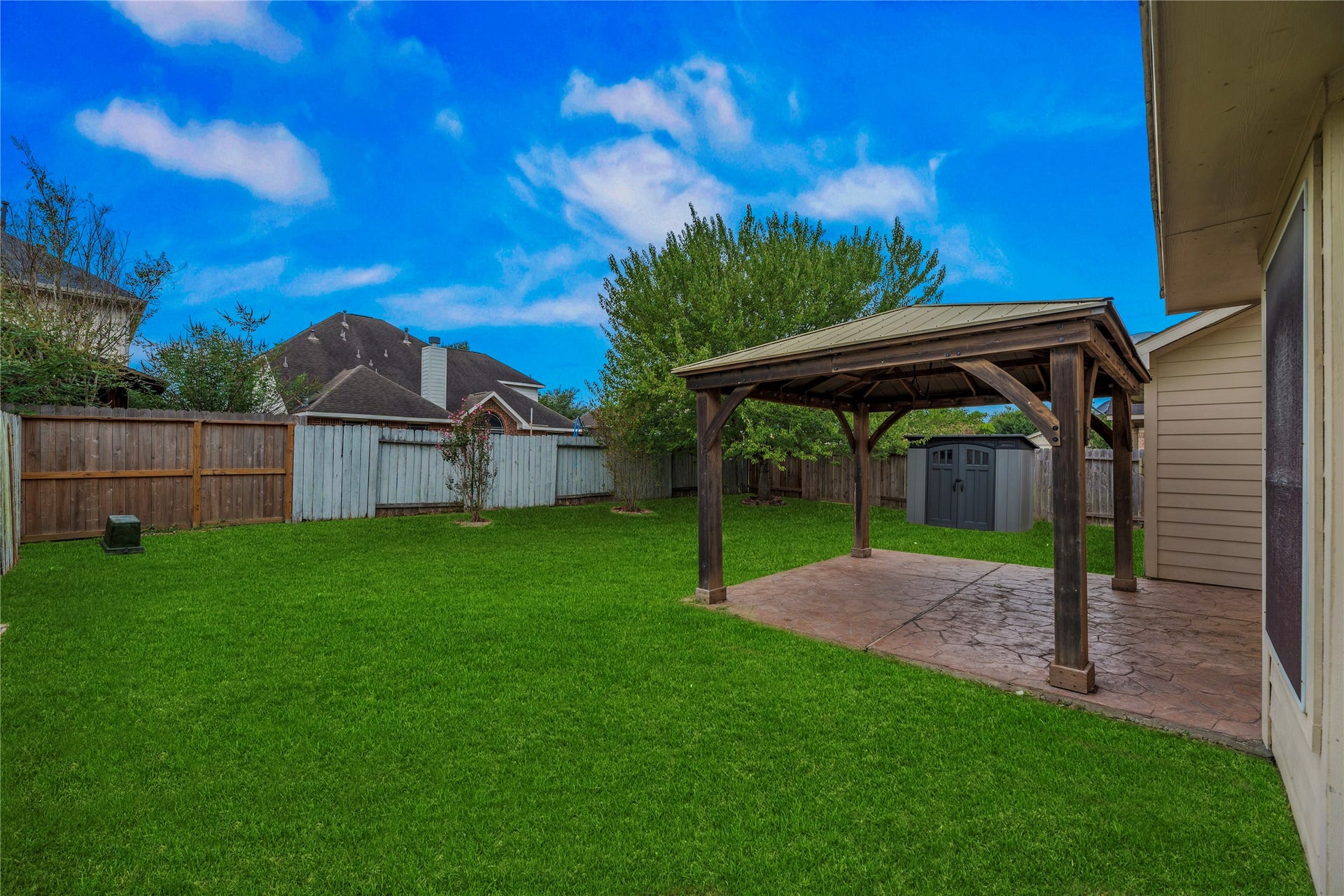 The gazebo-covered patio creates an outdoor sitting area, with lawn space beyond. Grass enhanced due to seasonality; see natural-lawn view.
