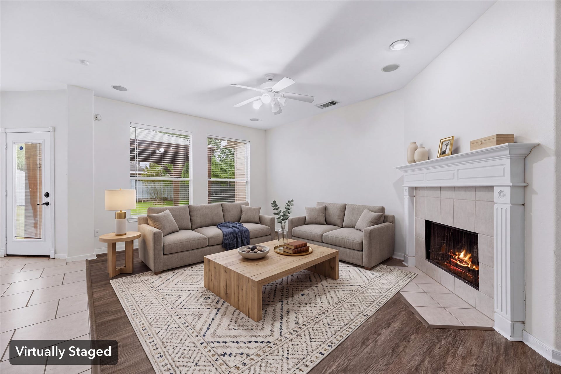 Virtually staged to show seating gathered around the fireplace, with backyard windows behind the sofa. Furniture shown is digital.