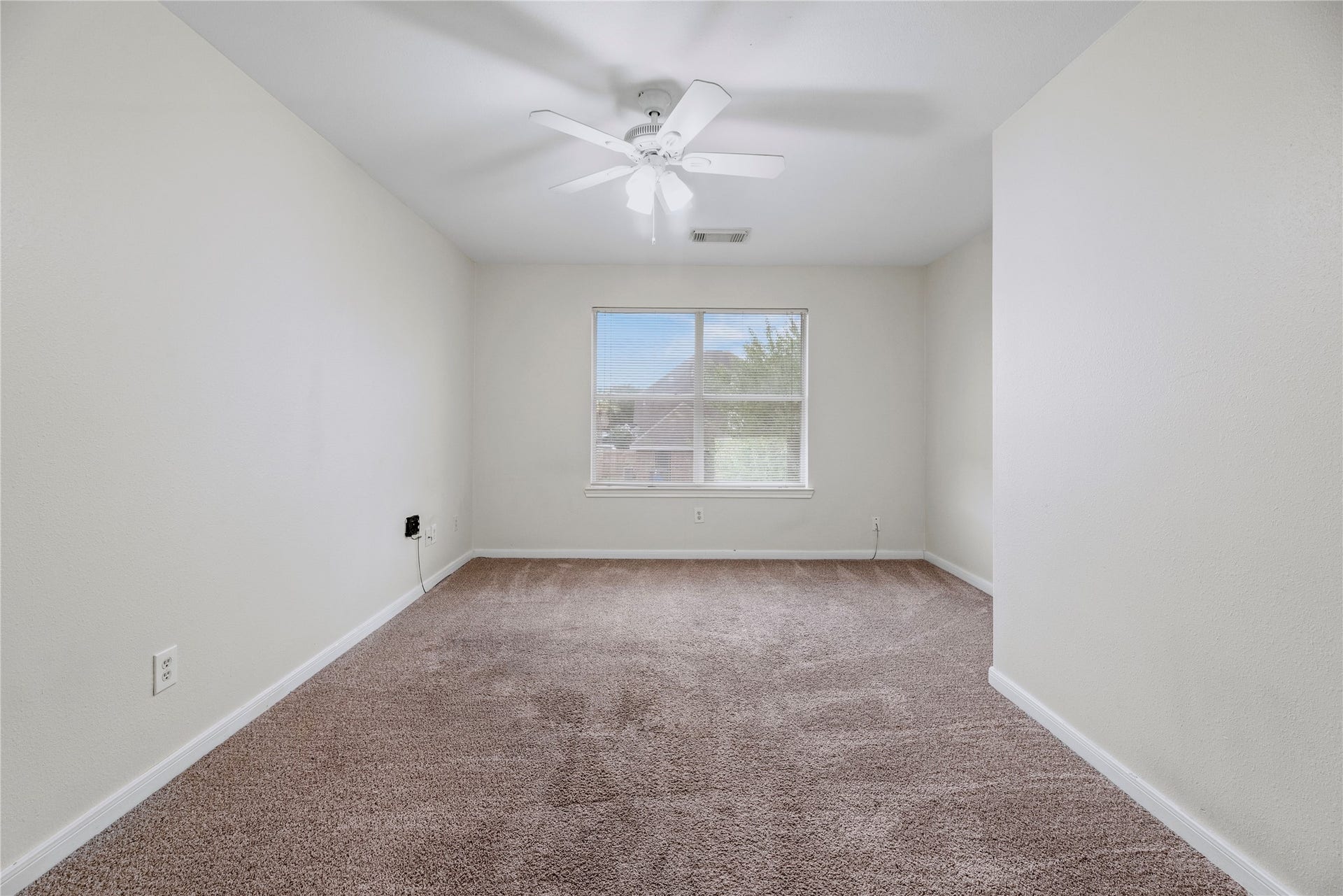 This secondary bedroom pairs a window and ceiling fan with open floor space, giving you room to arrange a bed, desk or your own preferred setup.