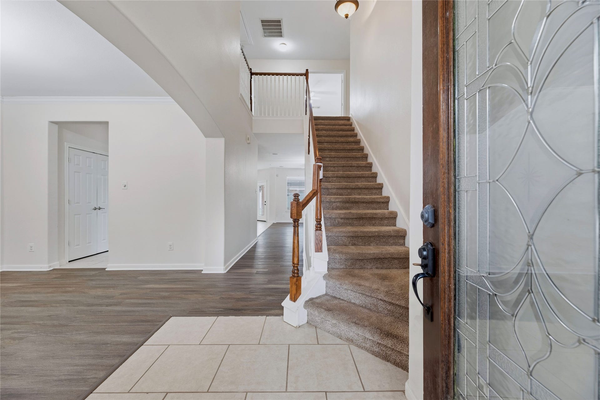 Step through the decorative-glass front door into a tall entry, with open sightlines to the front living area and a staircase leading upstairs.